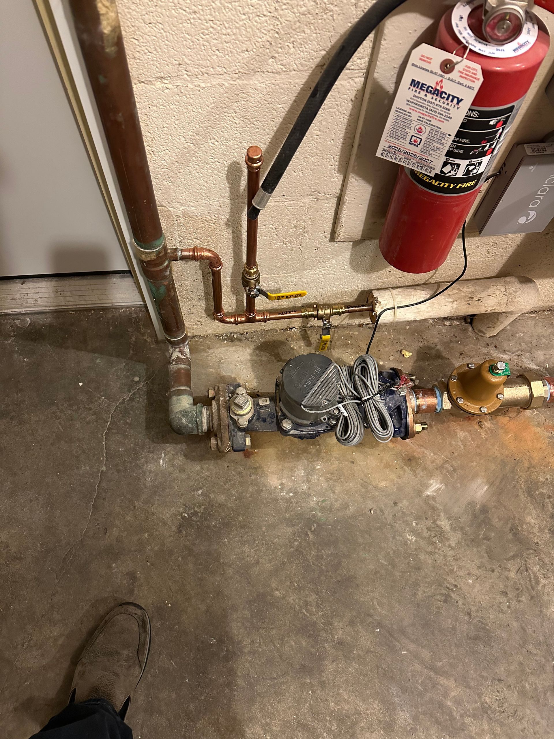 Fire extinguisher beside exposed plumbing and gas meter on a concrete floor.