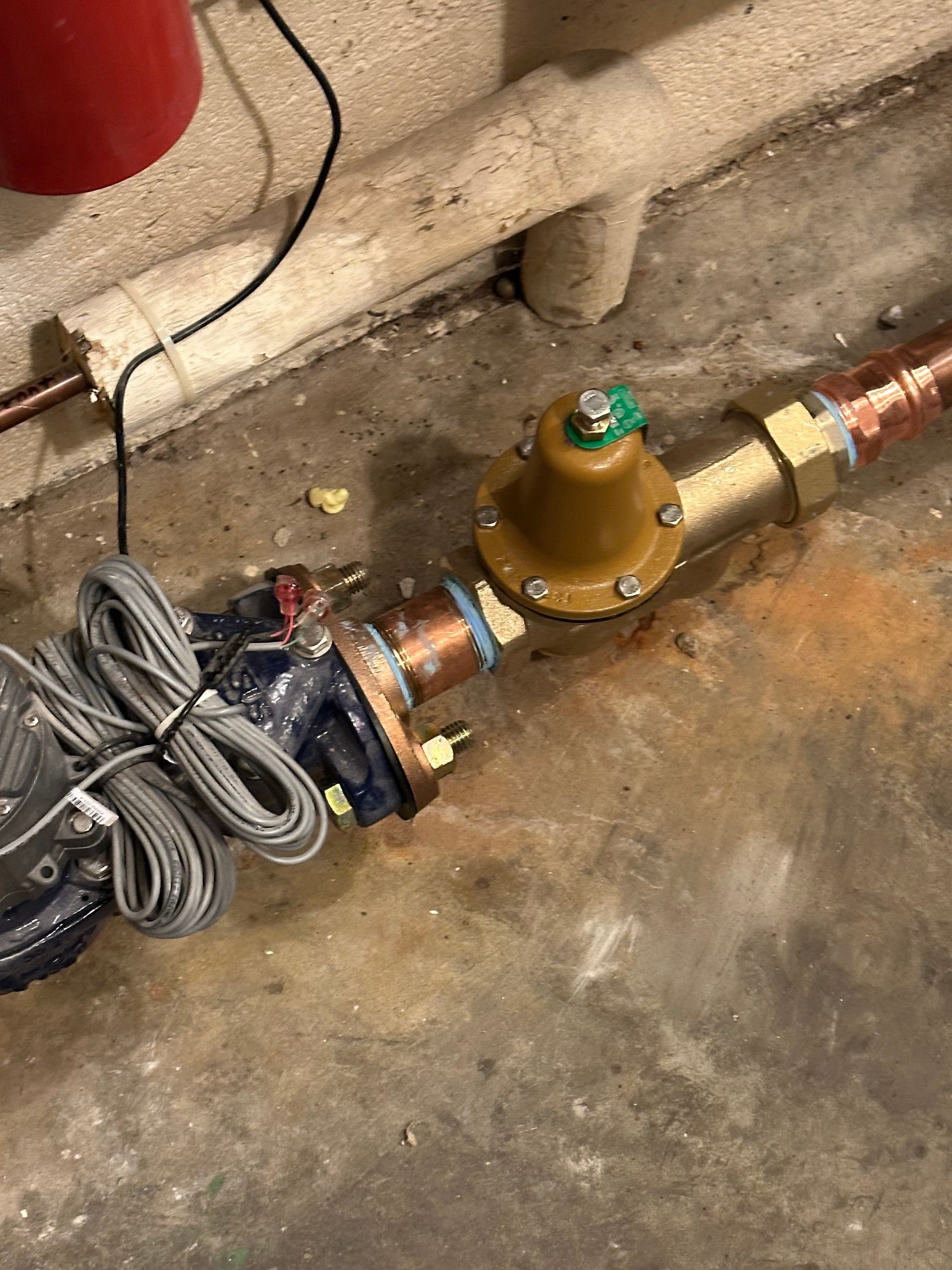 Pipe assembly with a gold pressure regulator and coiled cables on a concrete floor