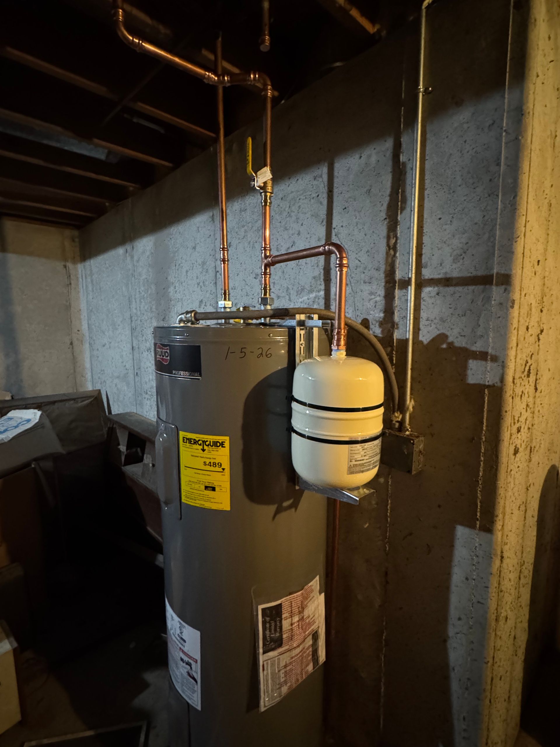 Water heater with expansion tank and copper pipes in a basement.