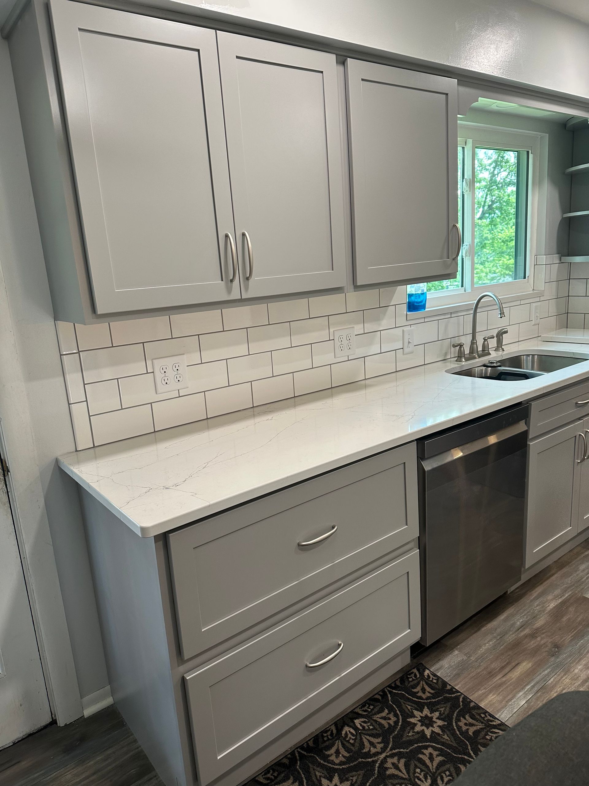 Modern kitchen with gray cabinets, white countertops, tiled backsplash, sink, dishwasher, and window view