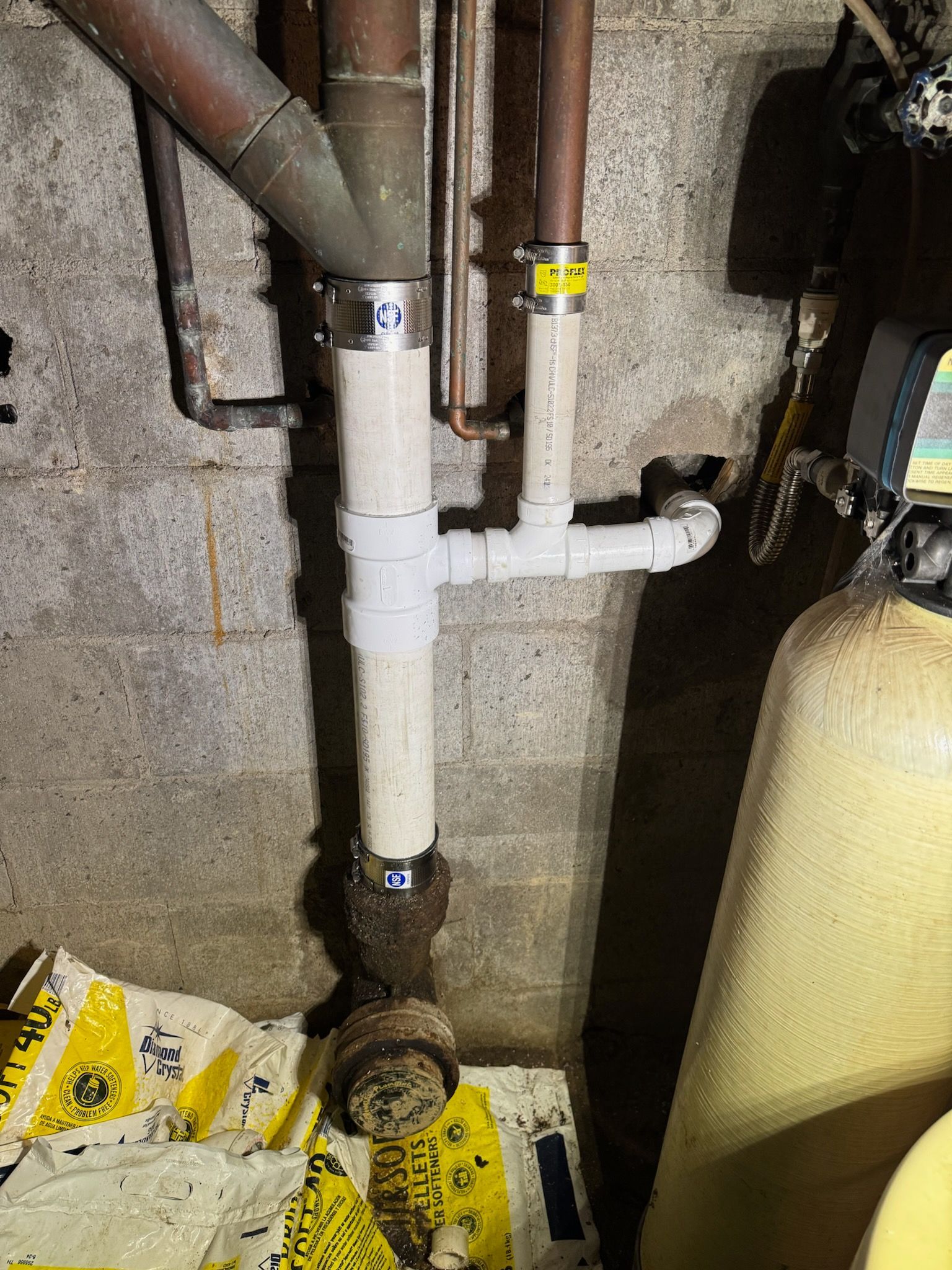 Basement plumbing with white PVC pipes, valves, and a pressure tank against a rough concrete wall