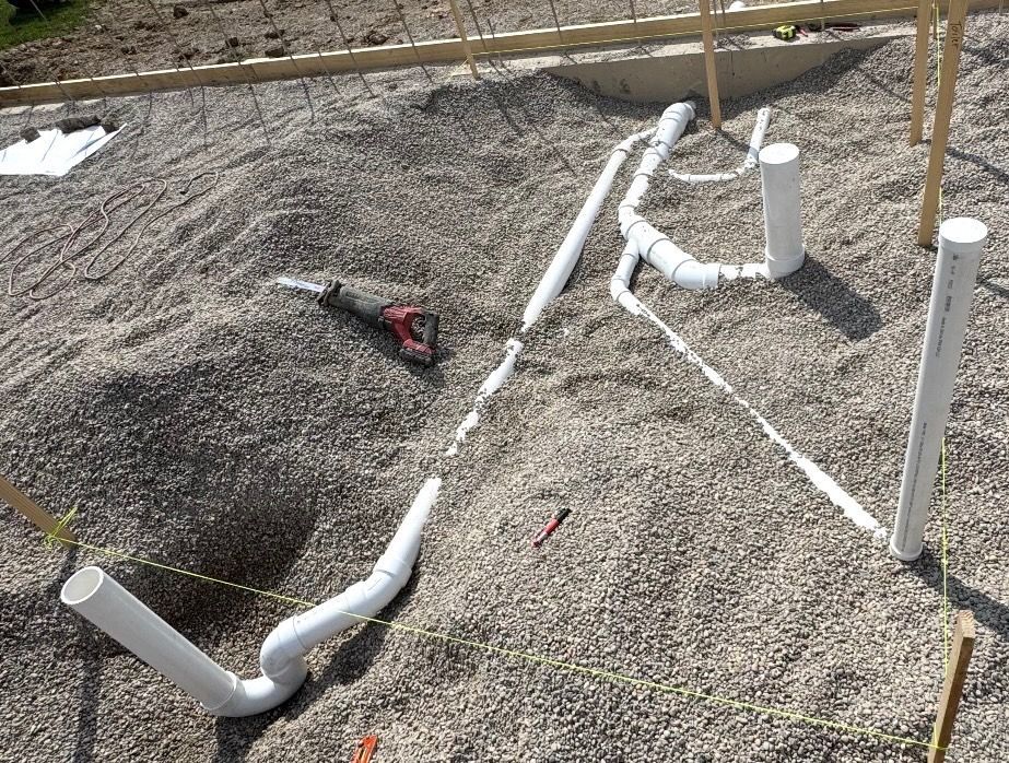 PVC pipes laid in gravel at a construction site, with a red tool nearby.