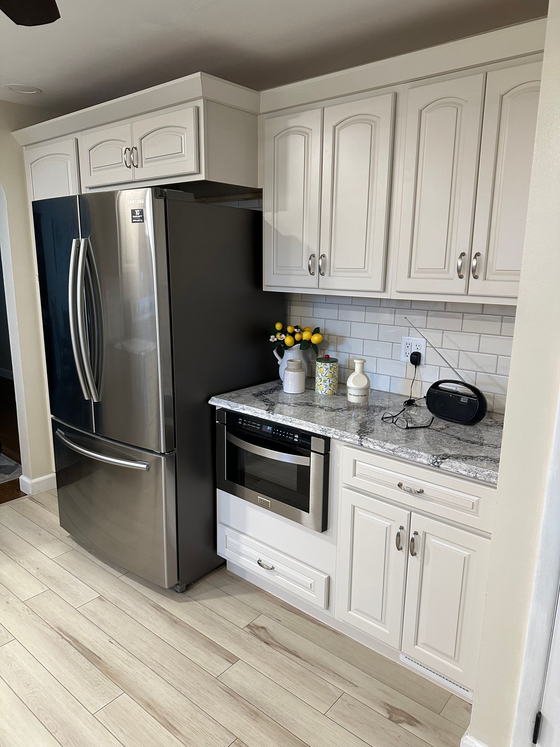 Modern kitchen with stainless steel refrigerator, white cabinets, granite counters, and a stove.