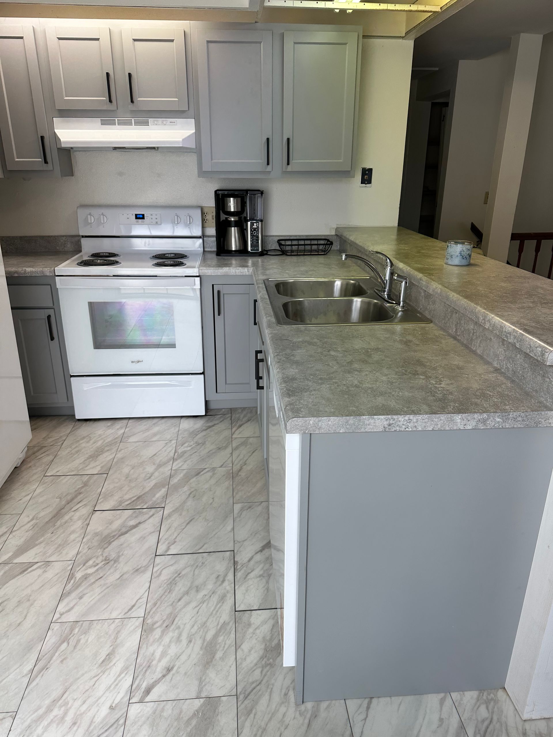 Small kitchen with white cabinets, gray countertops, white stove, and a double sink.