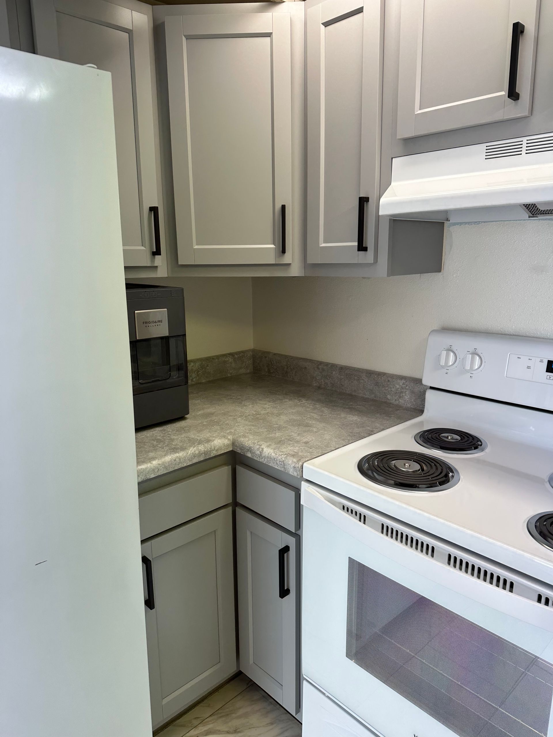 Small white kitchen corner with cabinets, countertop, refrigerator, stove, and coffee maker