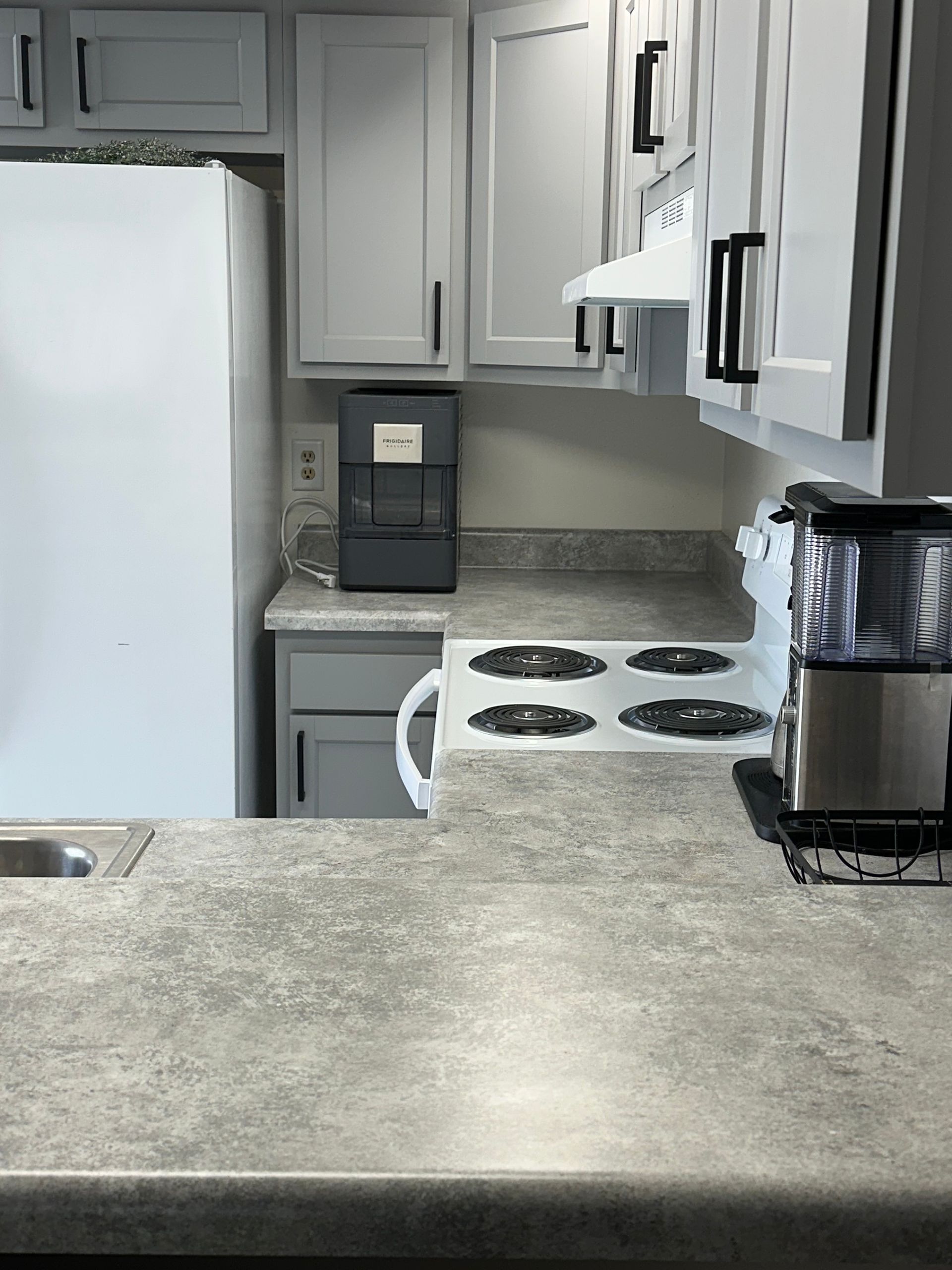 Small kitchen with white cabinets, white stove, refrigerator, and coffee maker on a gray countertop.