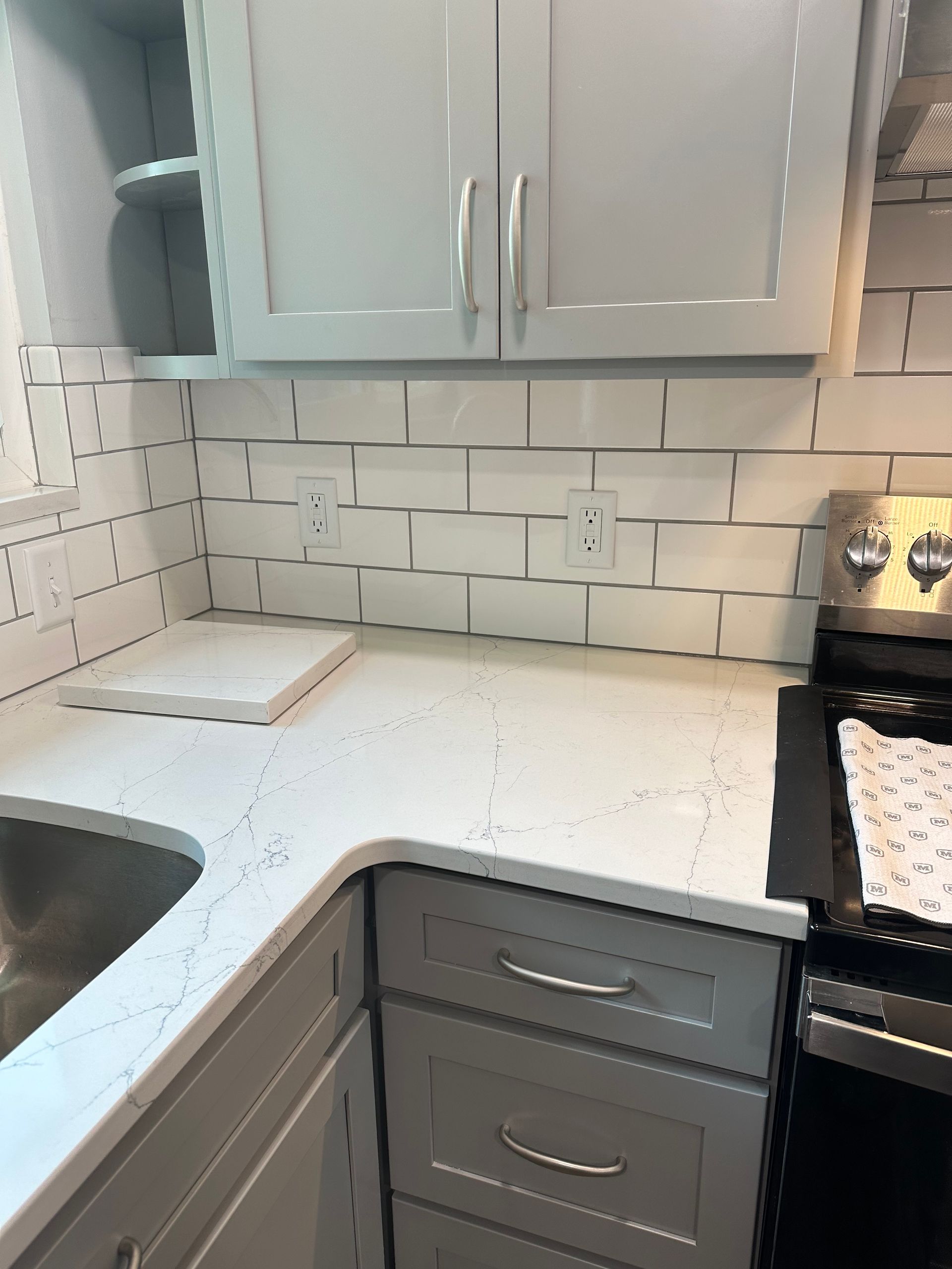Small kitchen corner with white cabinets, tile backsplash, and a black stove beside a sink and countertop.