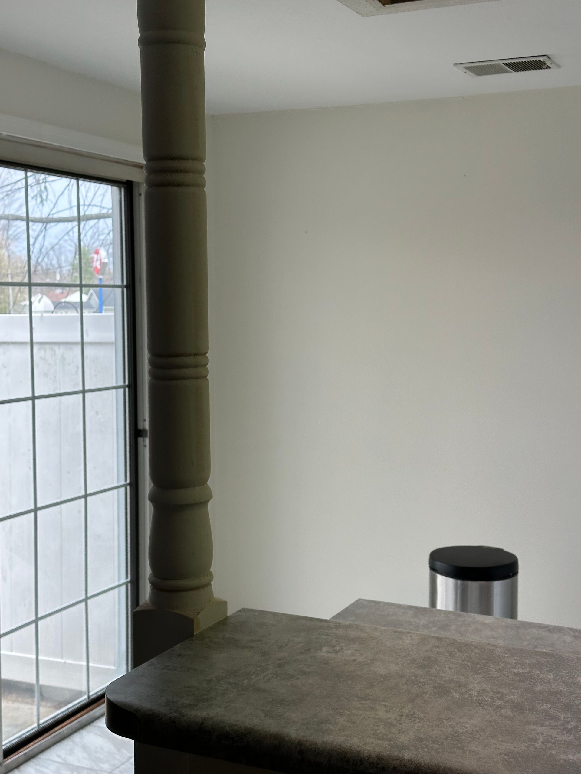 Small room with a large window, green support post, and a carpeted furniture surface in the foreground