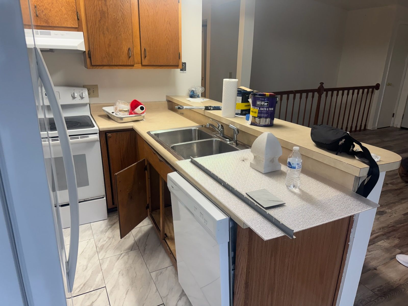 Small kitchen with a central sink island, wooden cabinets, stove, and staircase railing in the background