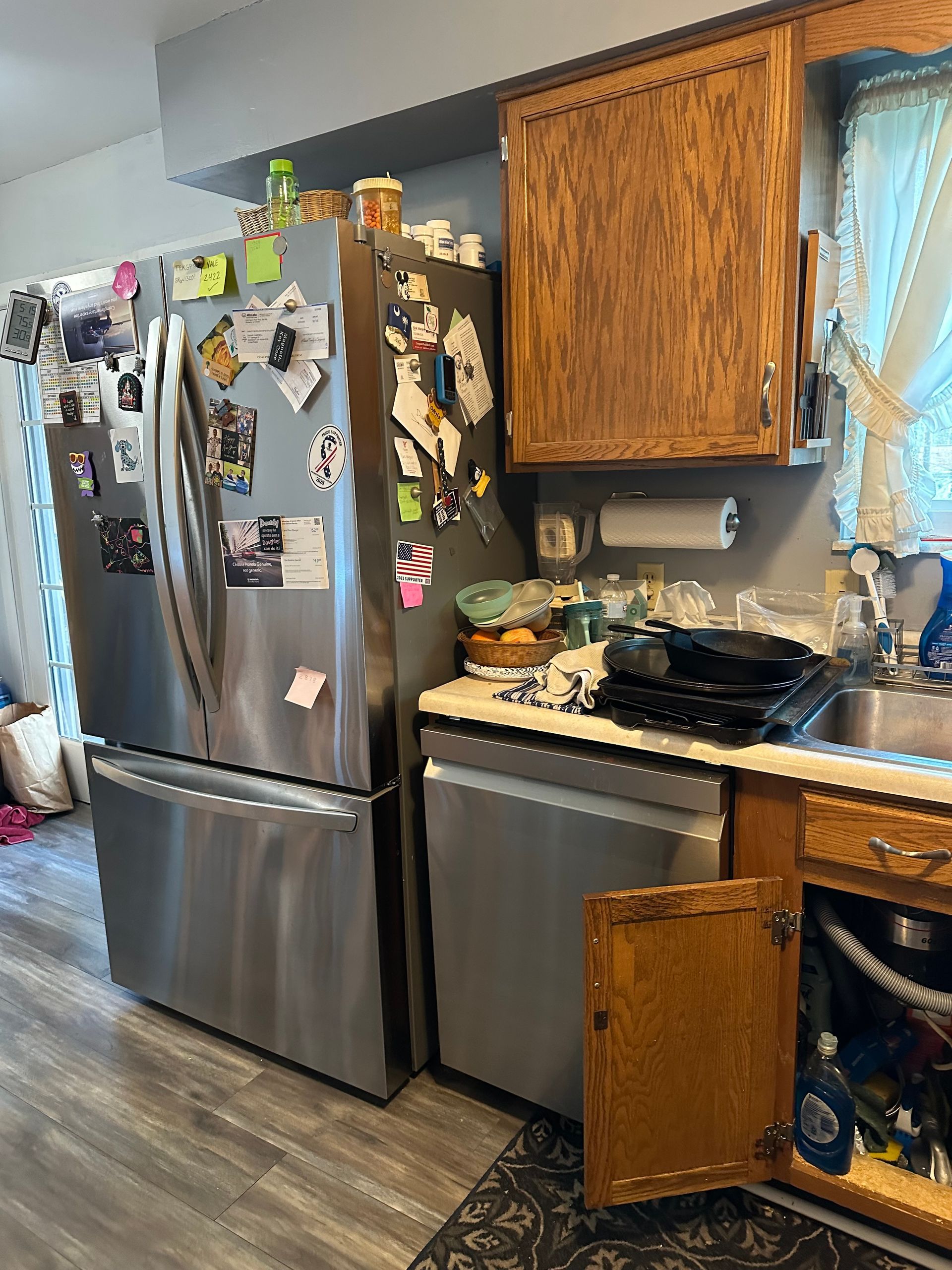 Kitchen with stainless steel fridge, cabinets, and sink, with an open cabinet door and magnets on the fridge