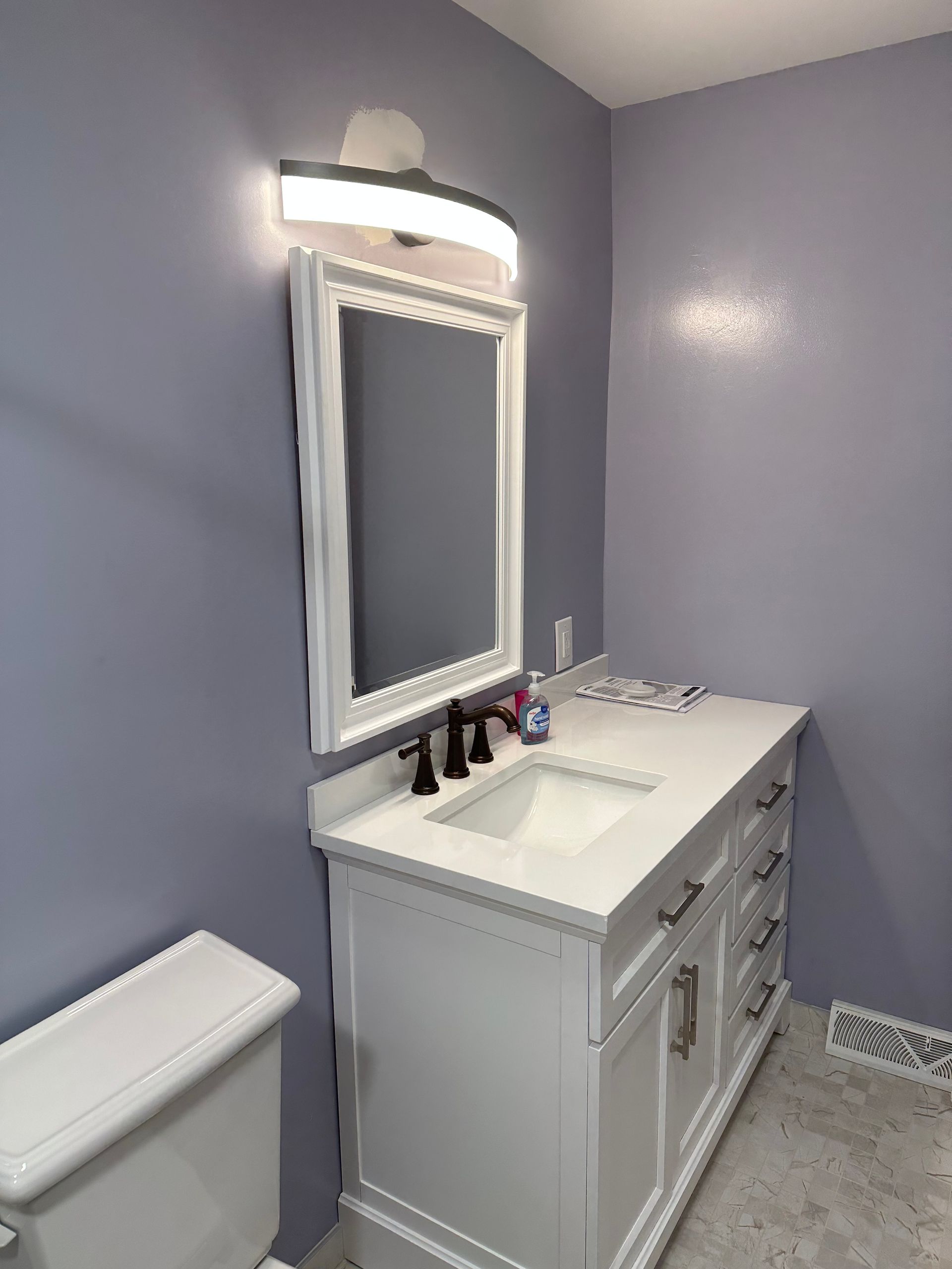 Small bathroom with lavender walls, white vanity, mirror, sink, light, and toilet visible.