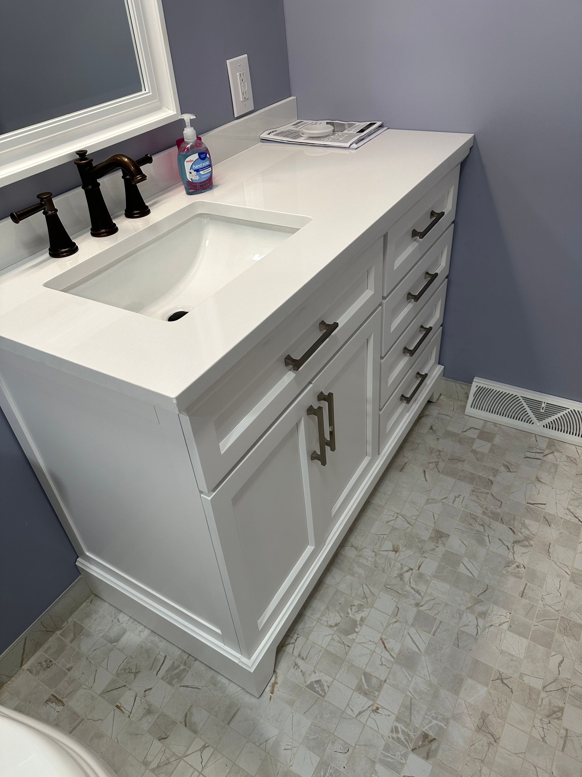 White bathroom vanity with double sink, black faucets, mirror, and gray floor tiles