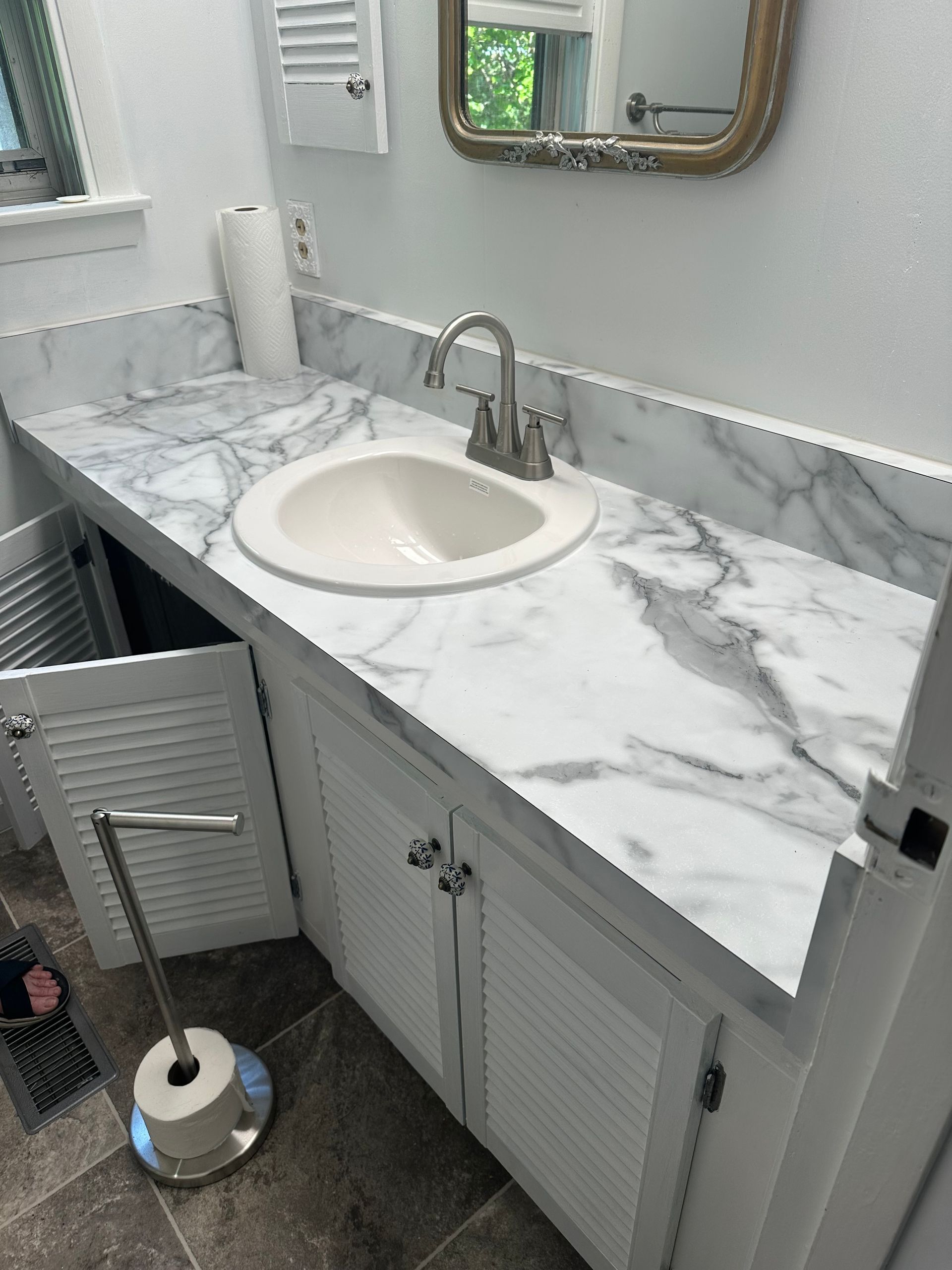 Bathroom vanity with white marble countertop, oval sink, chrome faucet, and mirrored cabinet above.