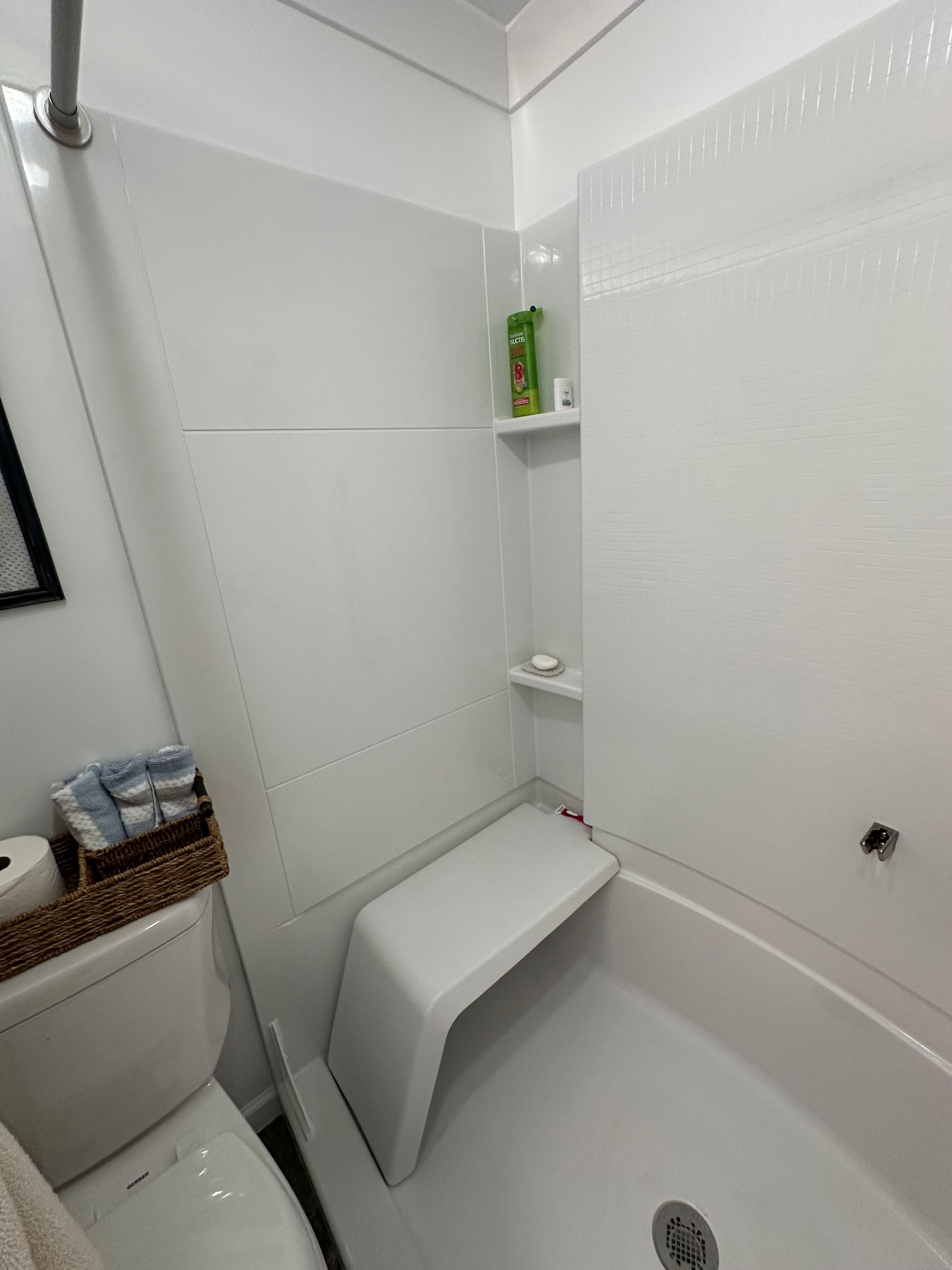 Small white bathroom with a bathtub, toilet, and corner shelves holding toiletries.