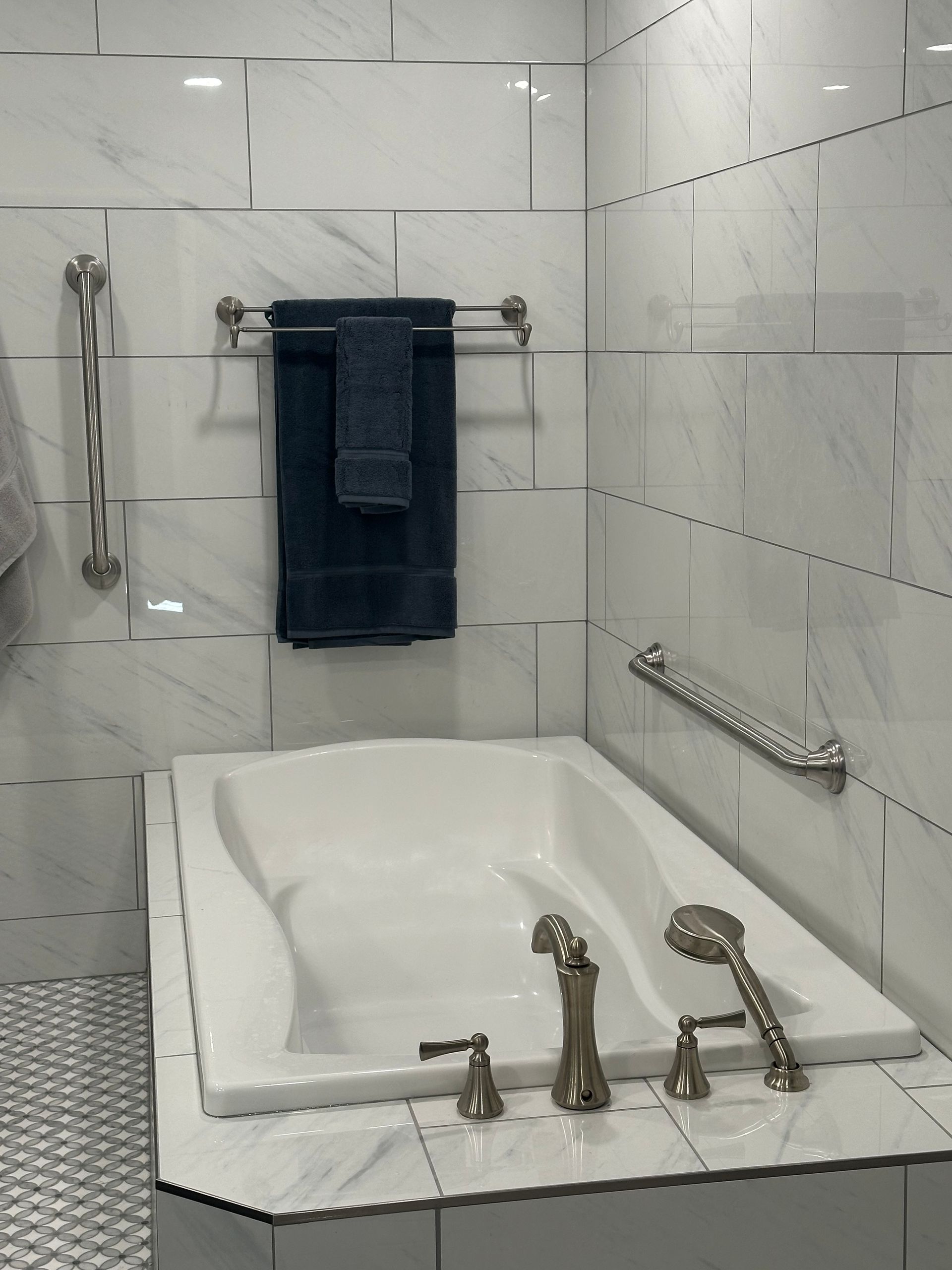 Bathroom with a white soaking tub, chrome fixtures, tiled walls, and a dark blue towel hanging above it