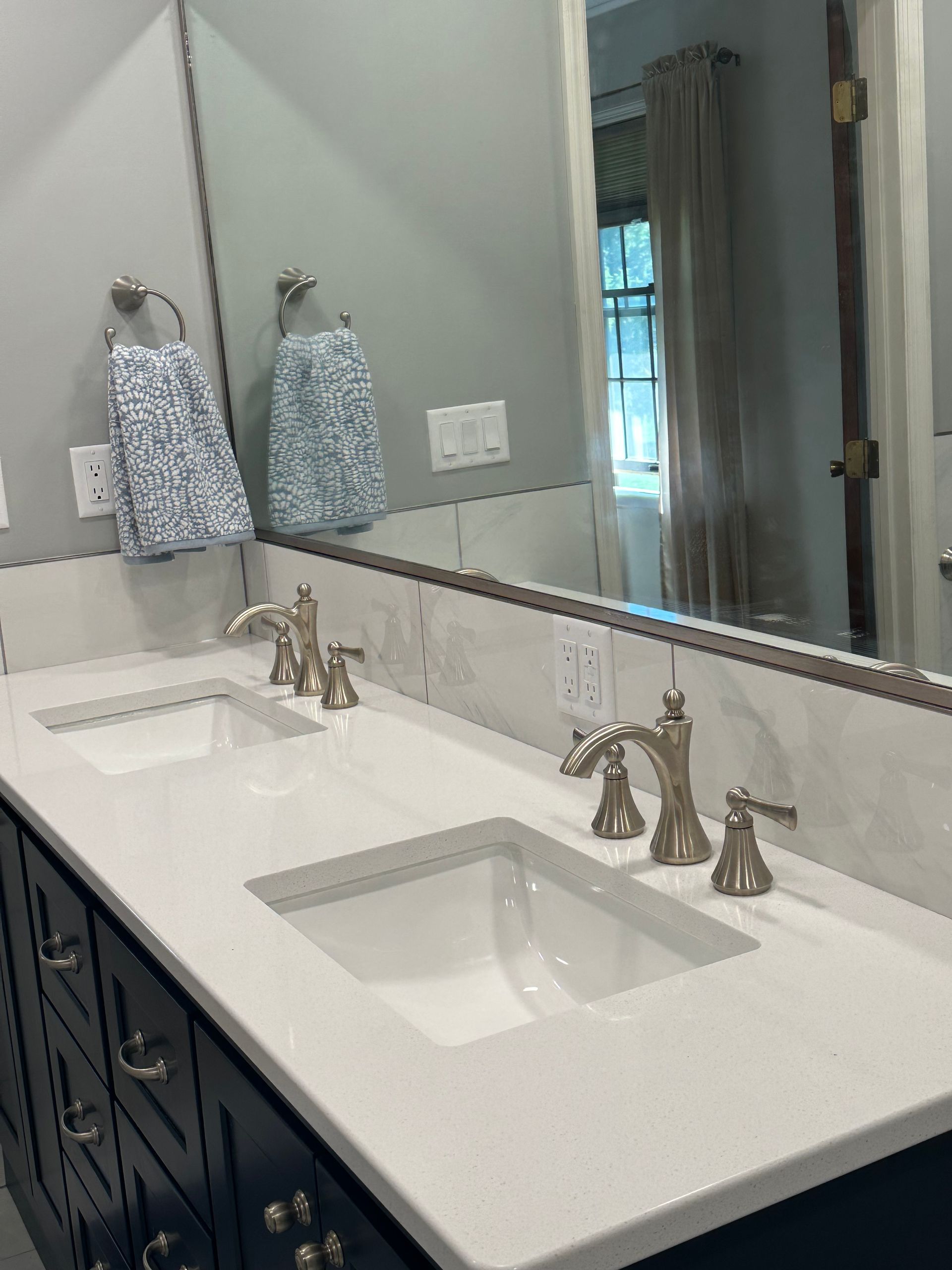 Modern bathroom vanity with double sinks, white countertop, dark cabinets, and large mirror.