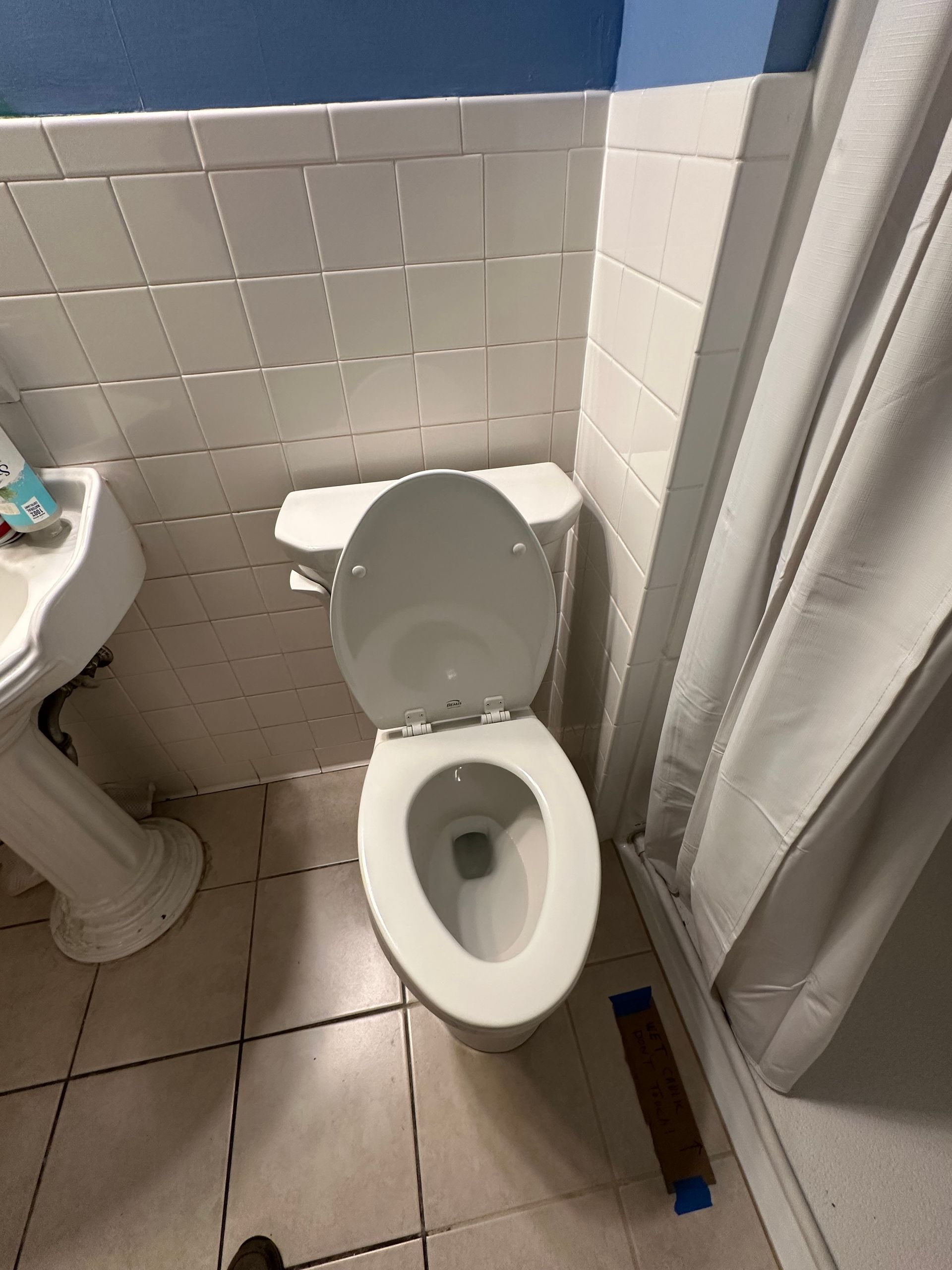 Small bathroom with a toilet, sink edge, shower curtain, and tiled walls/floor.