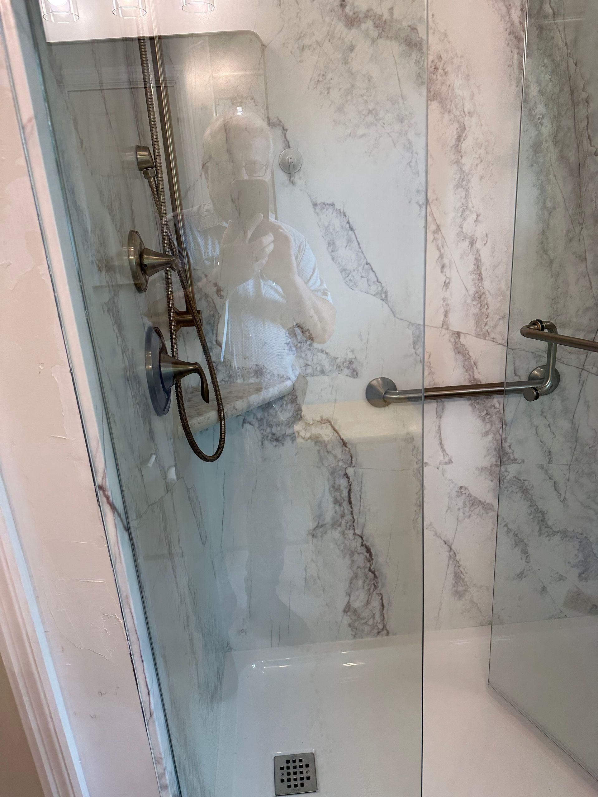 Glass shower with marble-look walls, chrome fixtures, and handheld showerhead.