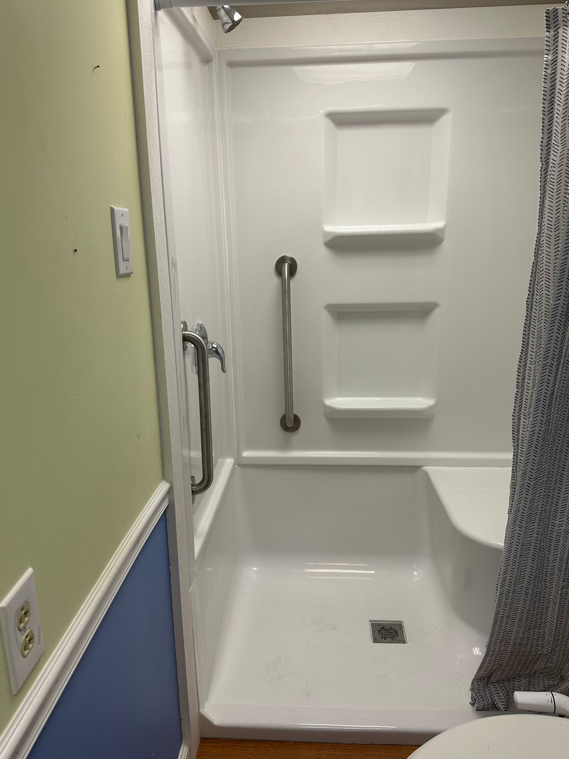 Accessible shower stall with grab bar, built-in shelves, and shower curtain in a small bathroom