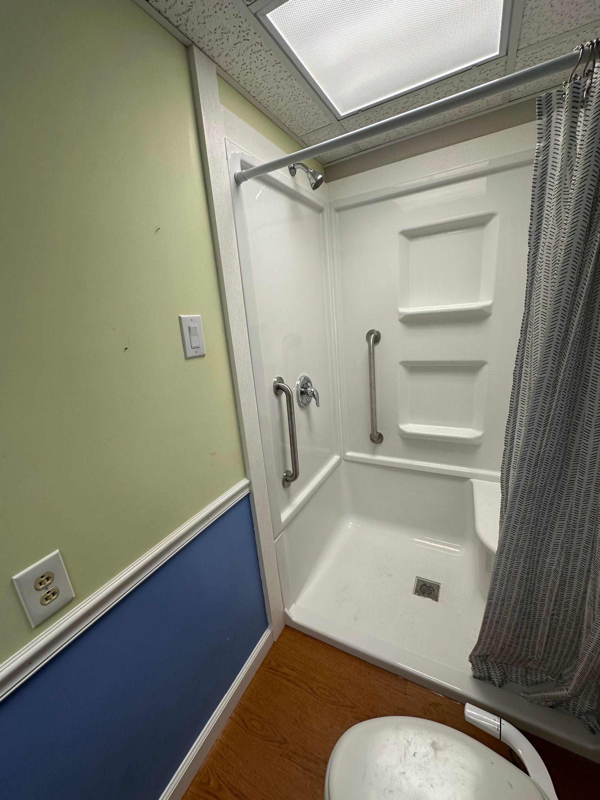 Accessible shower stall with white grab bars, curtain, and blue-green bathroom walls