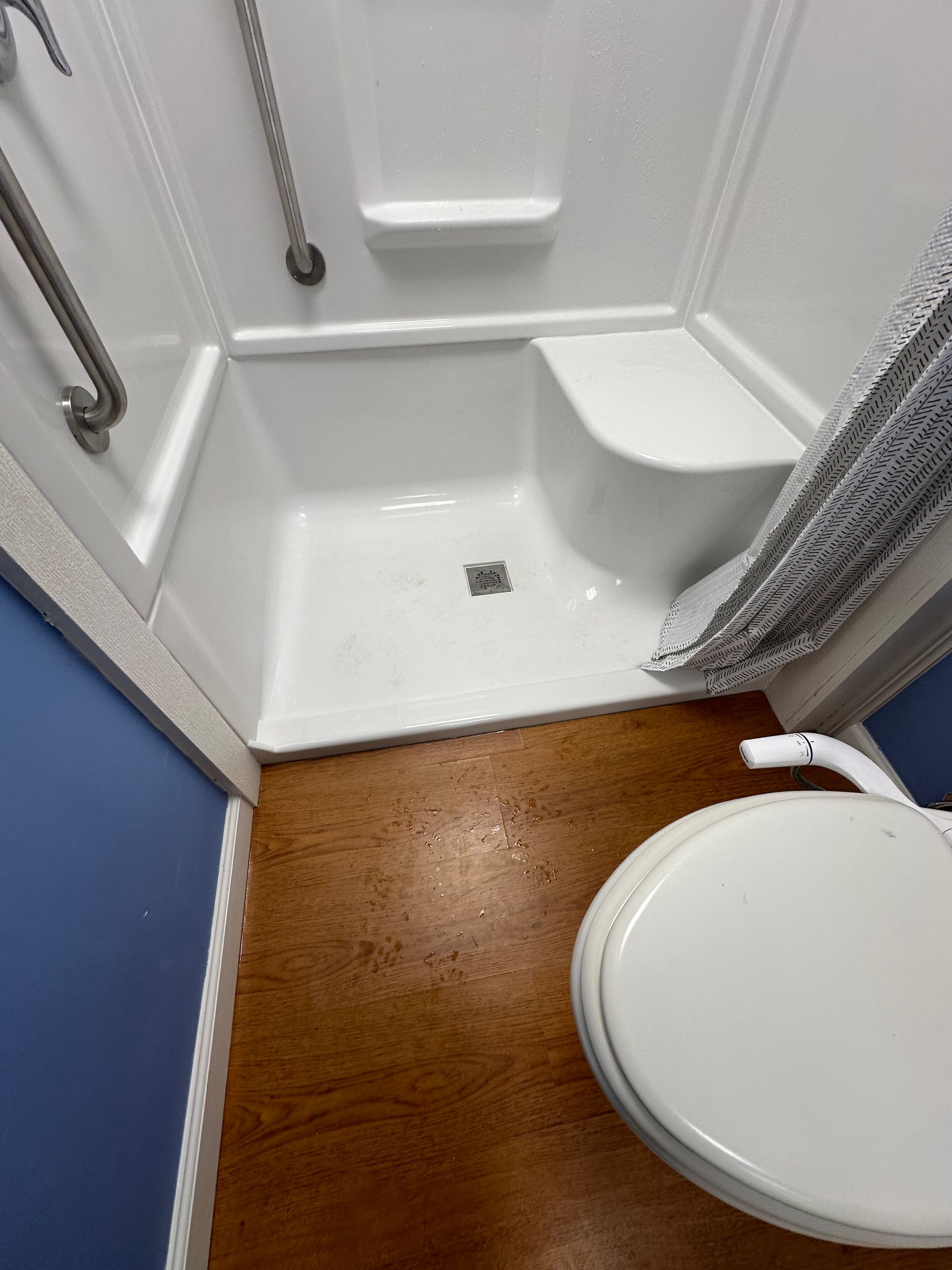 Compact shower stall with white fixtures, brown floor mat, and toilet edge in the foreground