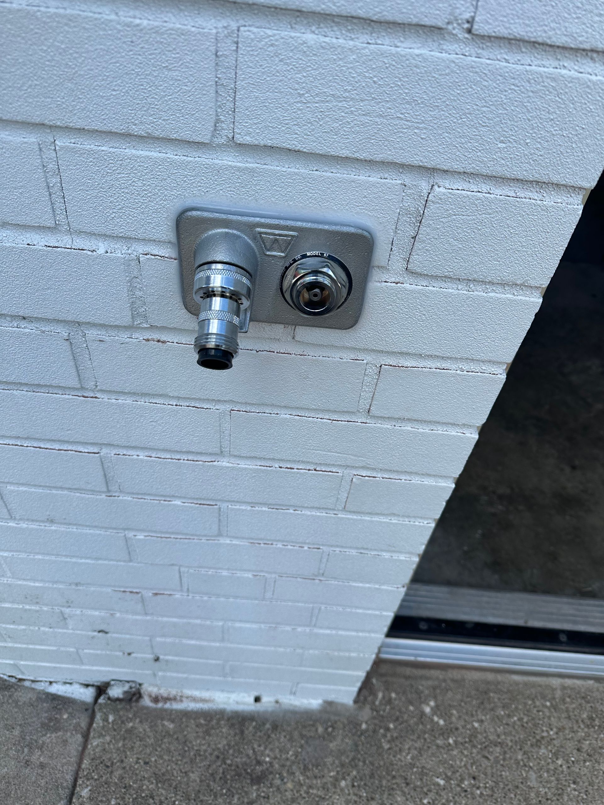 Close-up of a white brick wall with a metal faucet and round hose spigot near the floor.