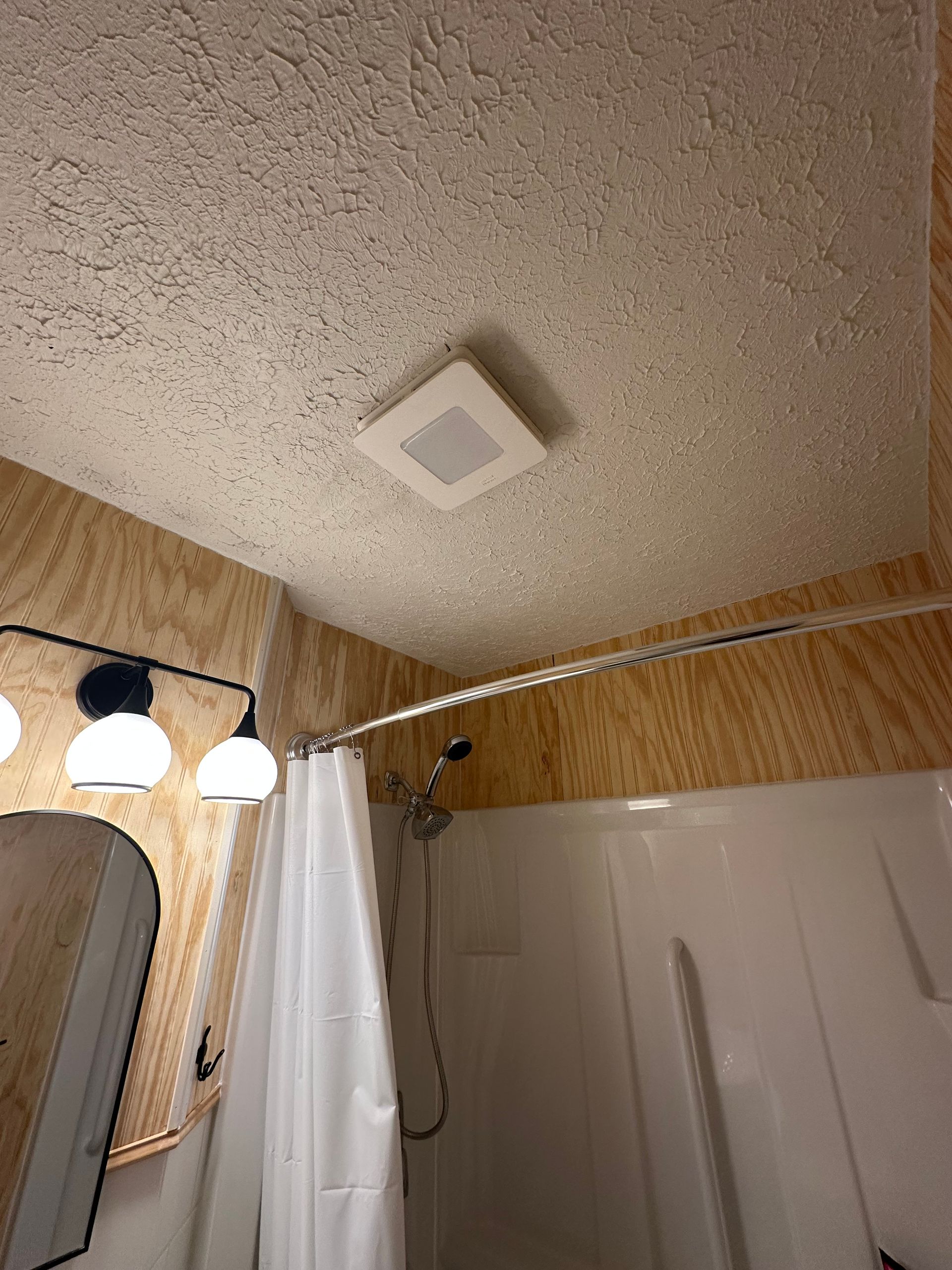 Bathroom ceiling with vent, shower curtain, mirror lights, and a partial door in view
