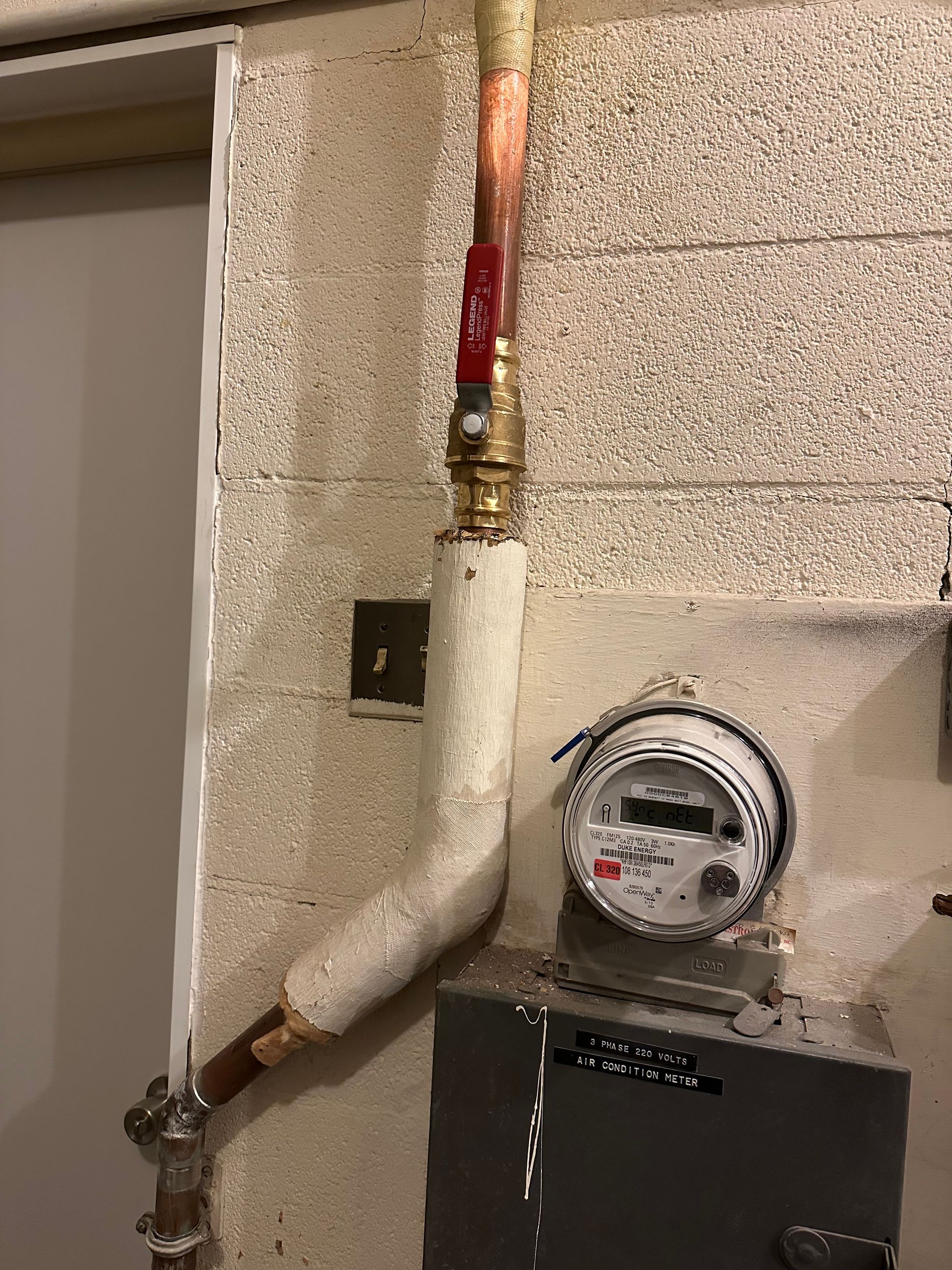 Gas meter and insulated copper pipes mounted on a cinder block wall.