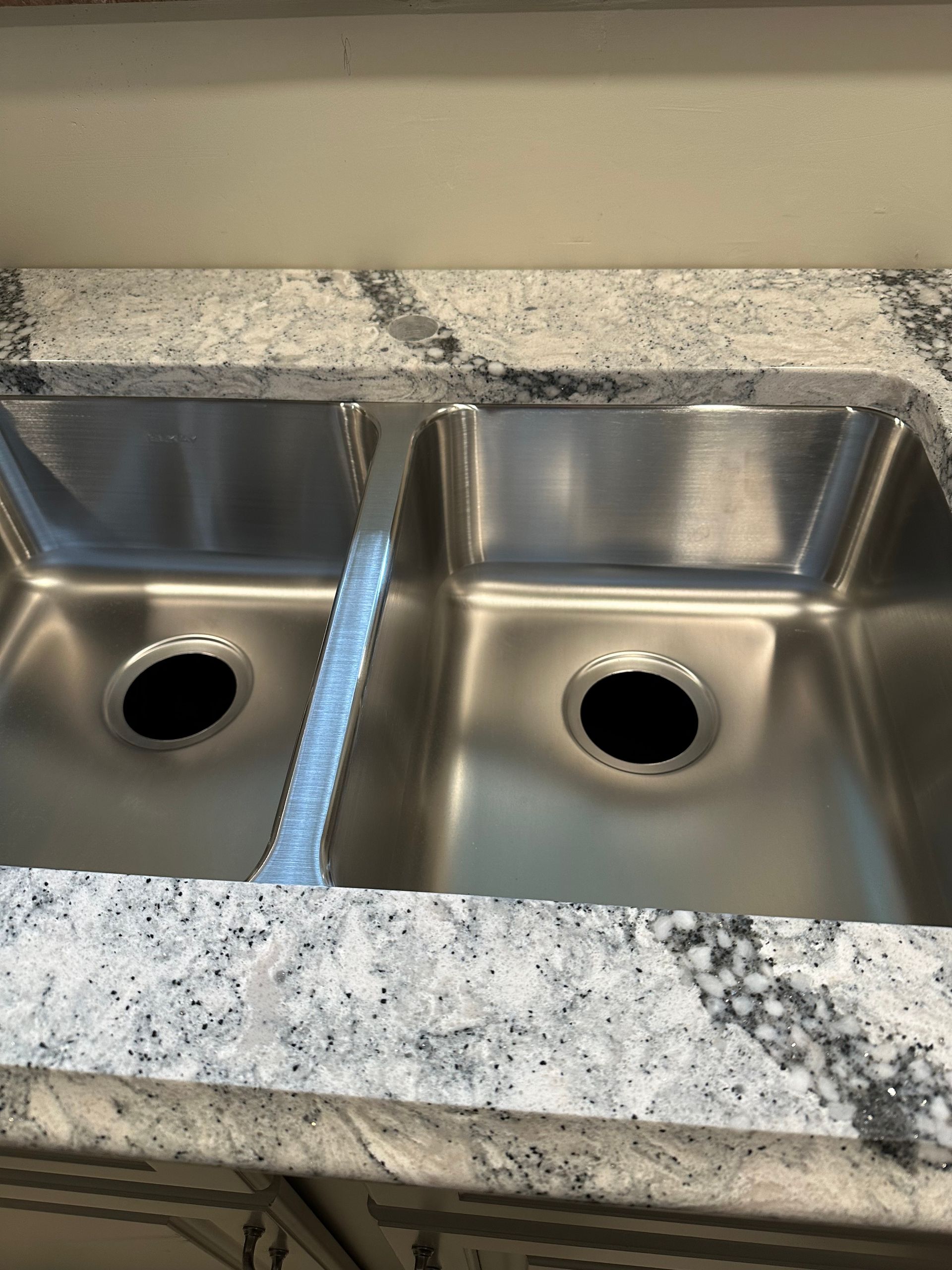 Double kitchen sink with a blue cleaning strip between basins and a speckled granite countertop