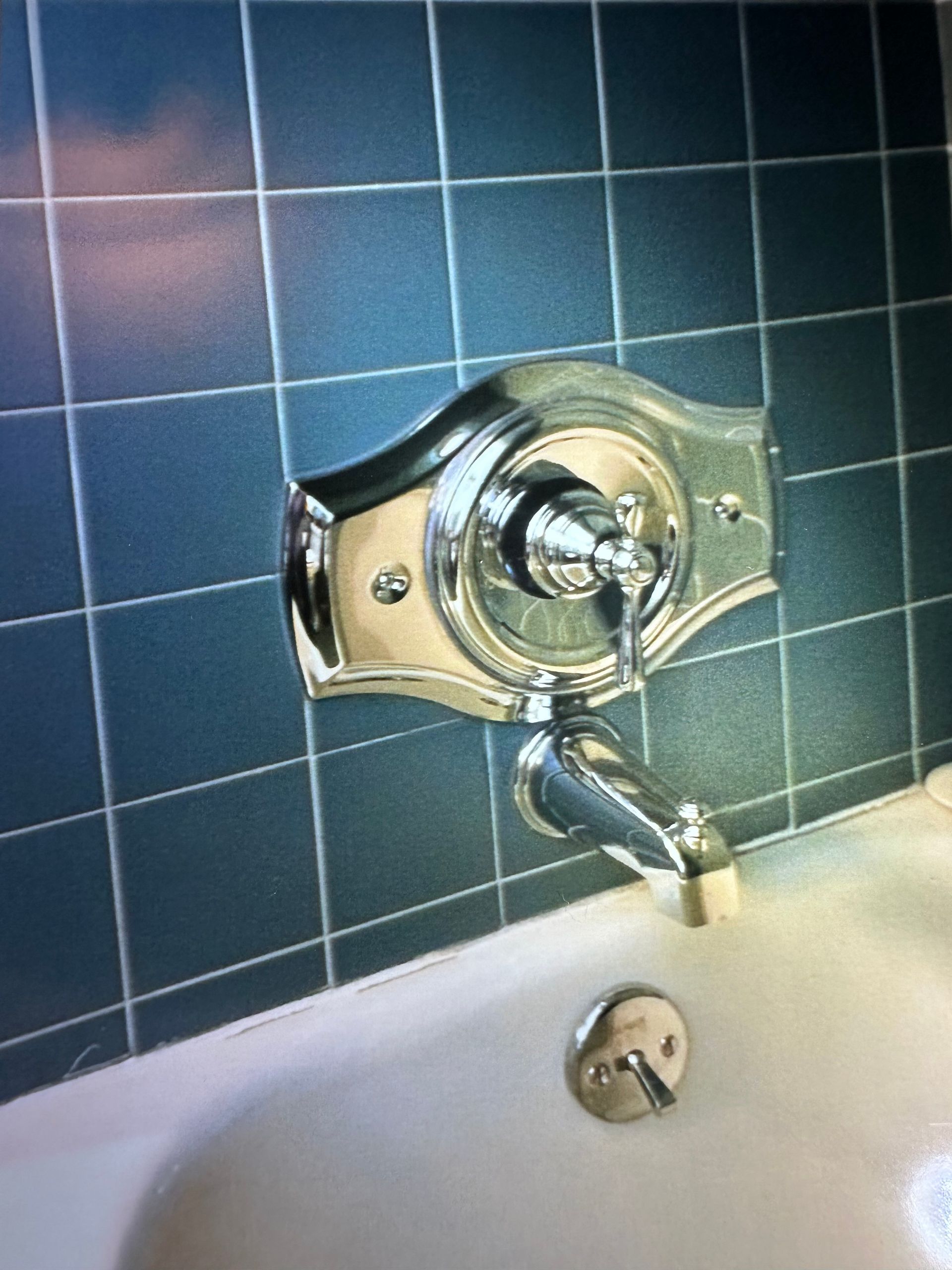 Chrome bathtub faucet and diverter on tiled bathroom wall above white tub
