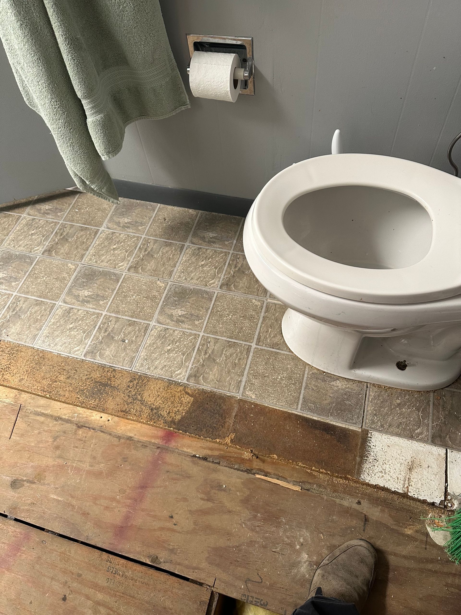 Bathroom with a white toilet, tiled floor, and a green towel hanging beside it.