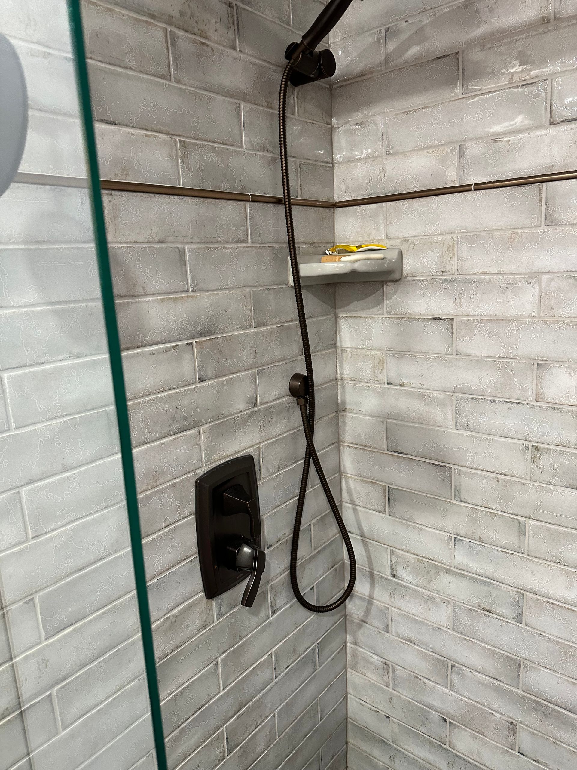 Shower corner with white brick walls, black showerhead hose, and a wall-mounted black control panel