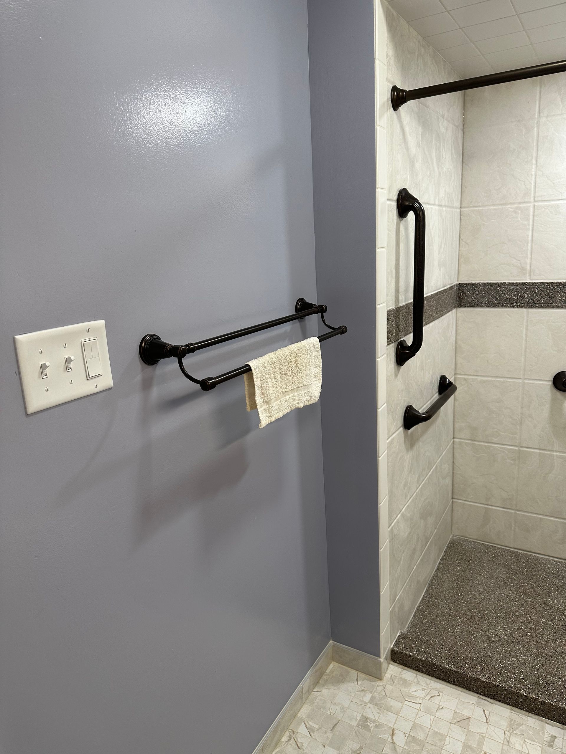Accessible bathroom with grab bars, towel ring, and walk-in shower beside a gray wall
