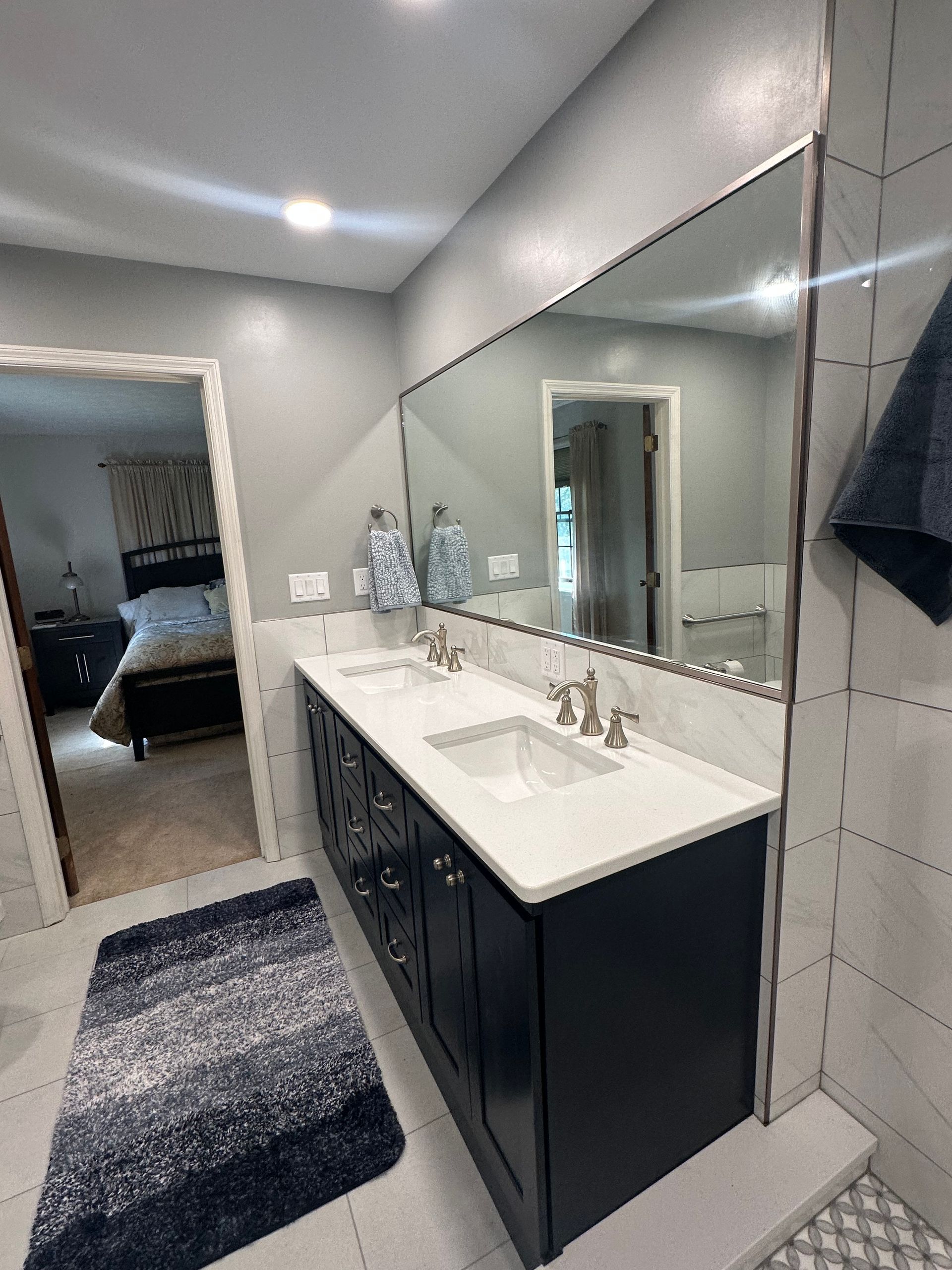 Modern bathroom with black vanity, white countertop, large mirror, and gray rug