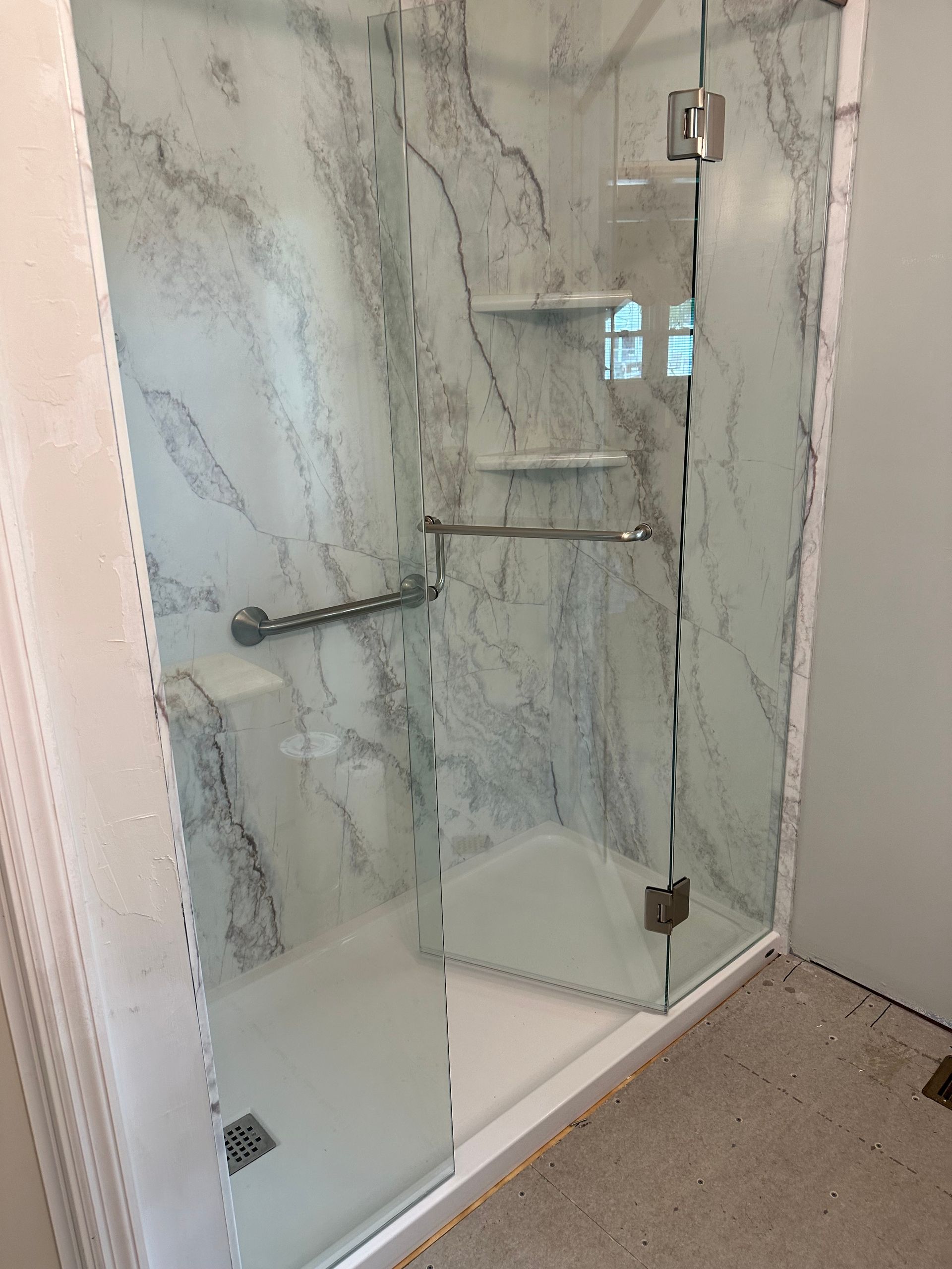 Glass shower enclosure with chrome shelves and a white base in a tiled bathroom
