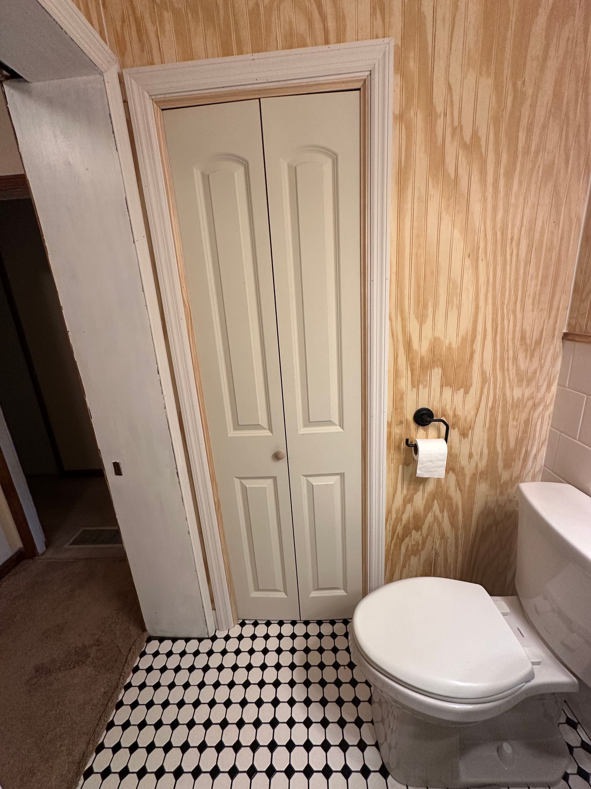 Small bathroom with toilet, closed closet door, and black-and-white checkered floor.