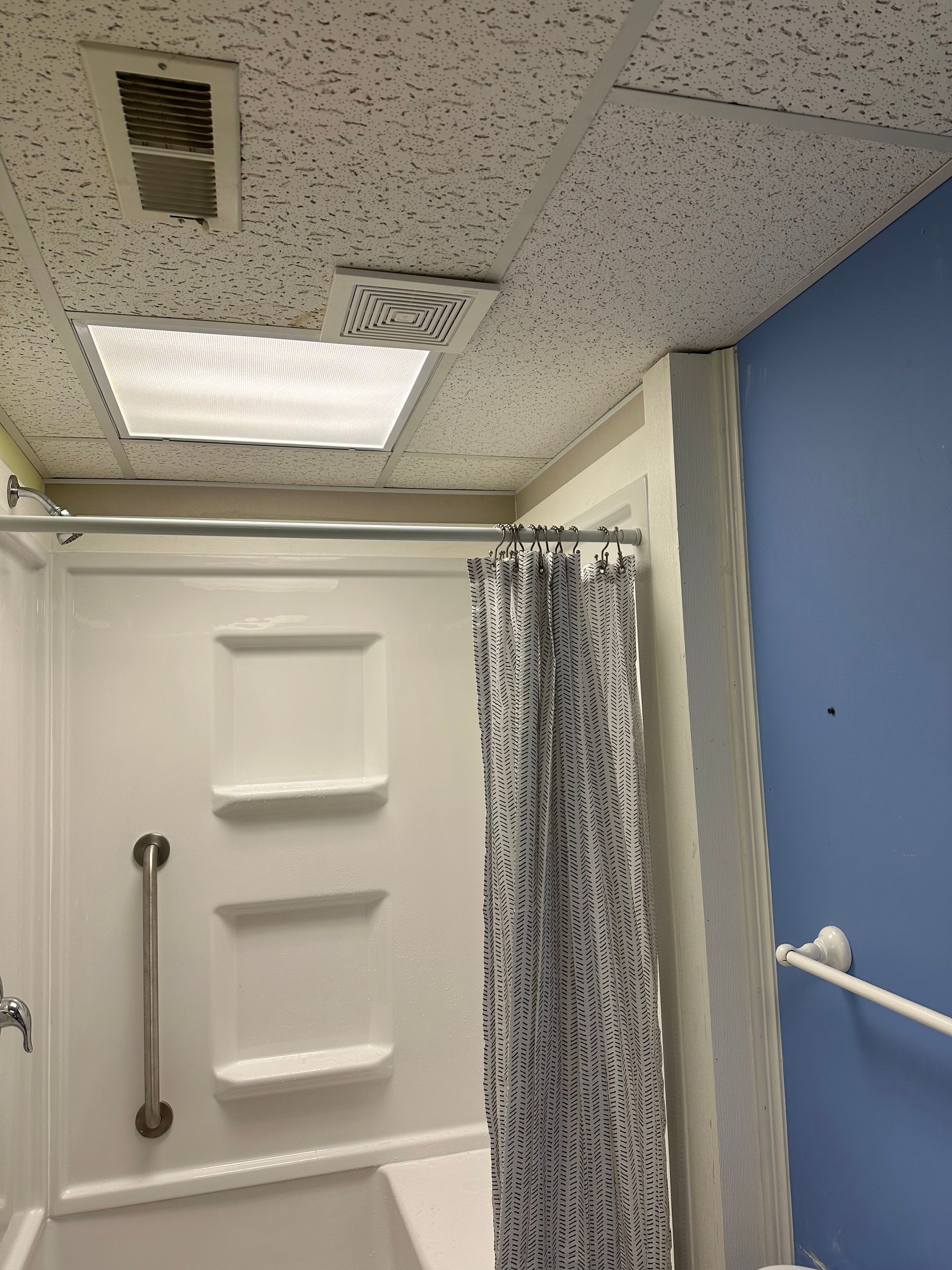 Accessible bathroom shower with white door, patterned curtain, and blue wall under a ceiling light