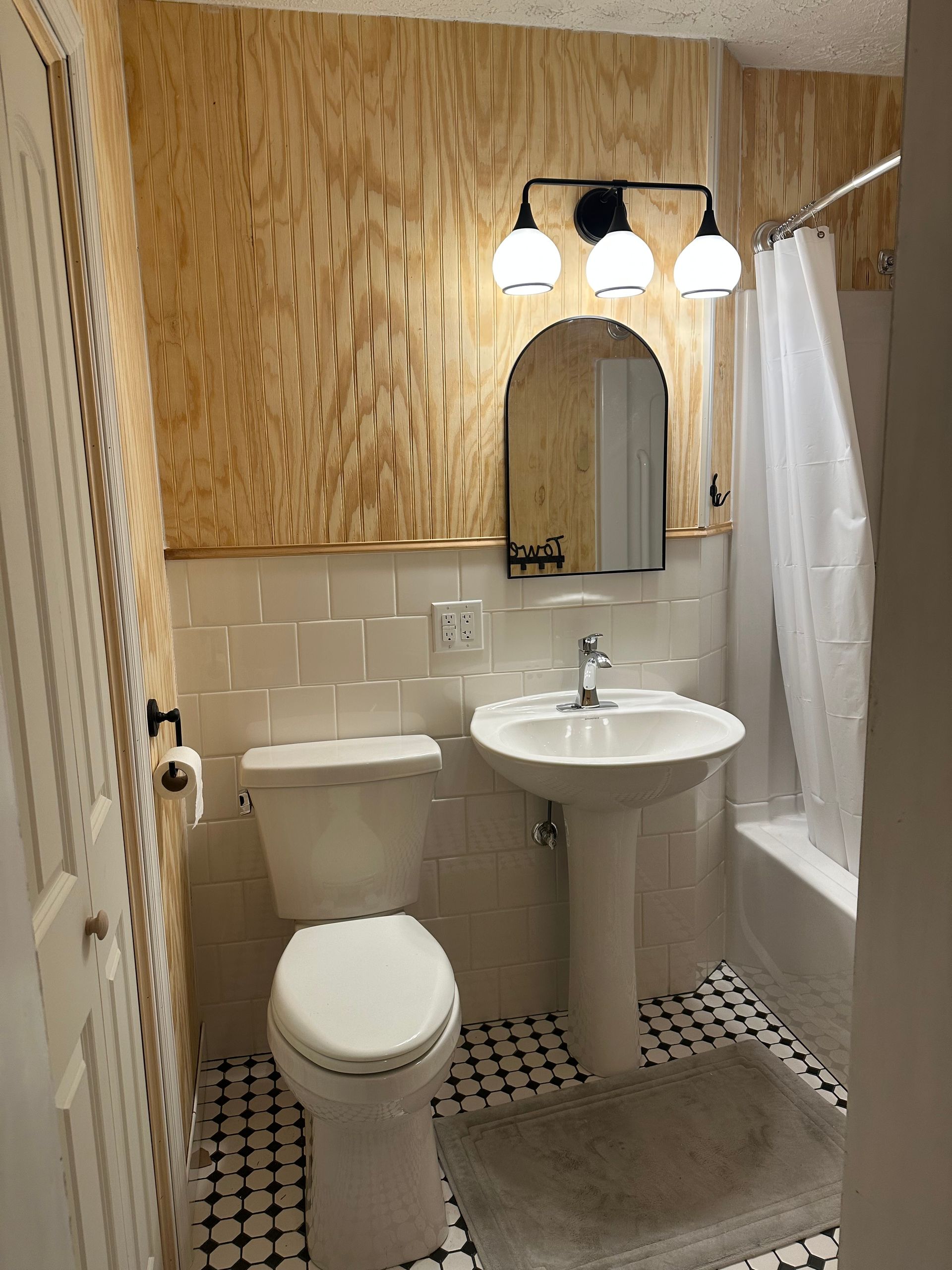 Small bathroom with toilet, pedestal sink, shower curtain, mirror, and woven wall decor.