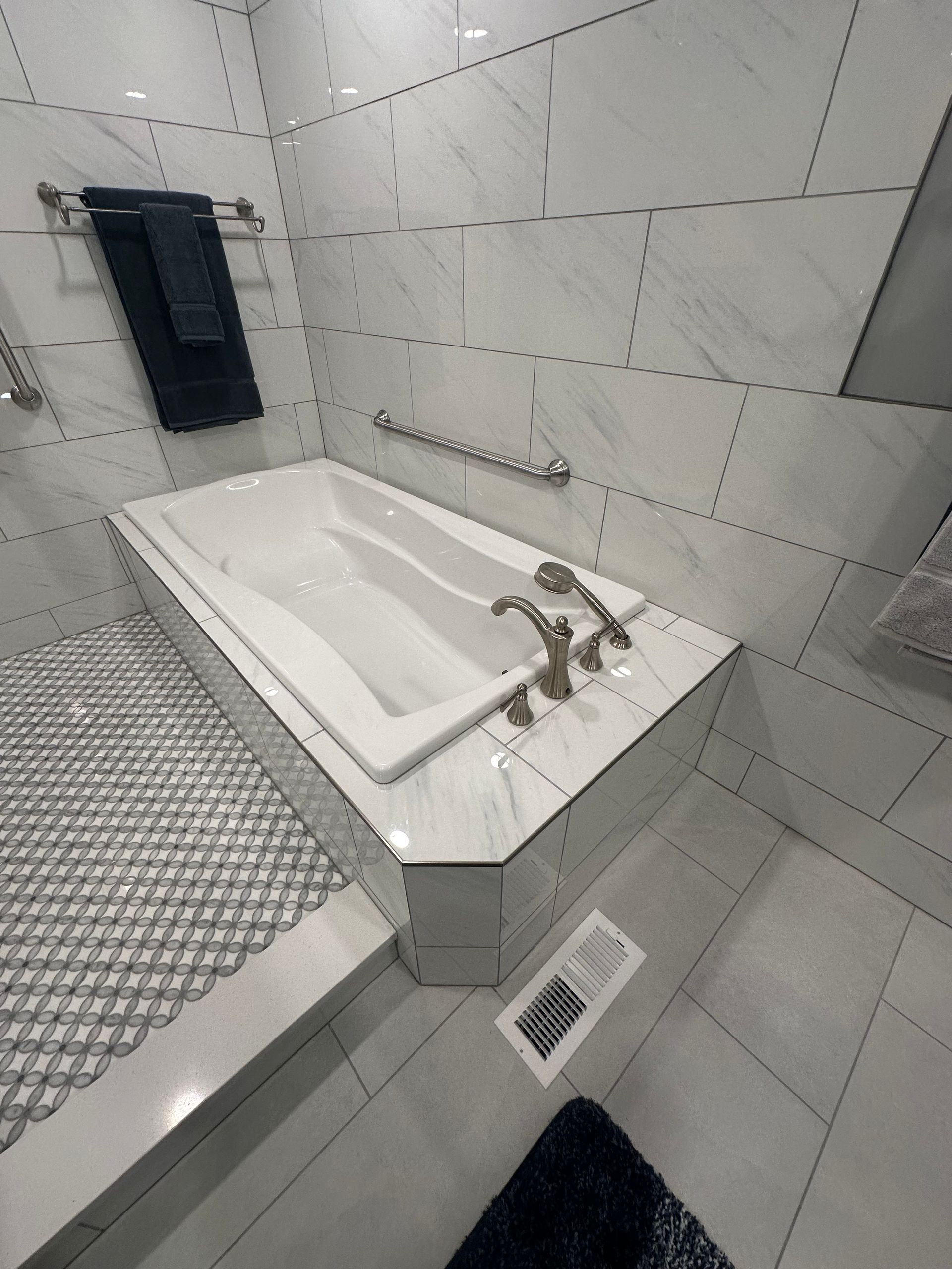 Modern tiled bathroom with a white bathtub, chrome faucet, shower towel, and diamond-plate floor.