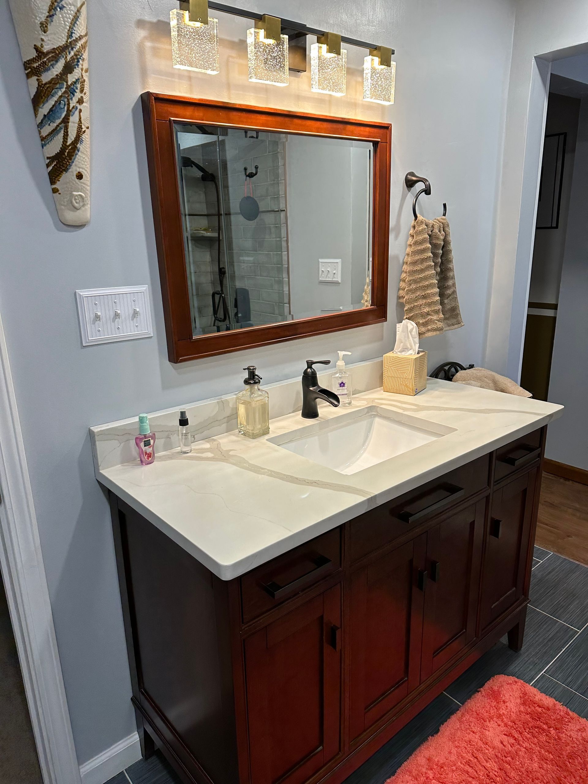 Bathroom vanity with mirror, white countertop, dark wood cabinet, and red rug