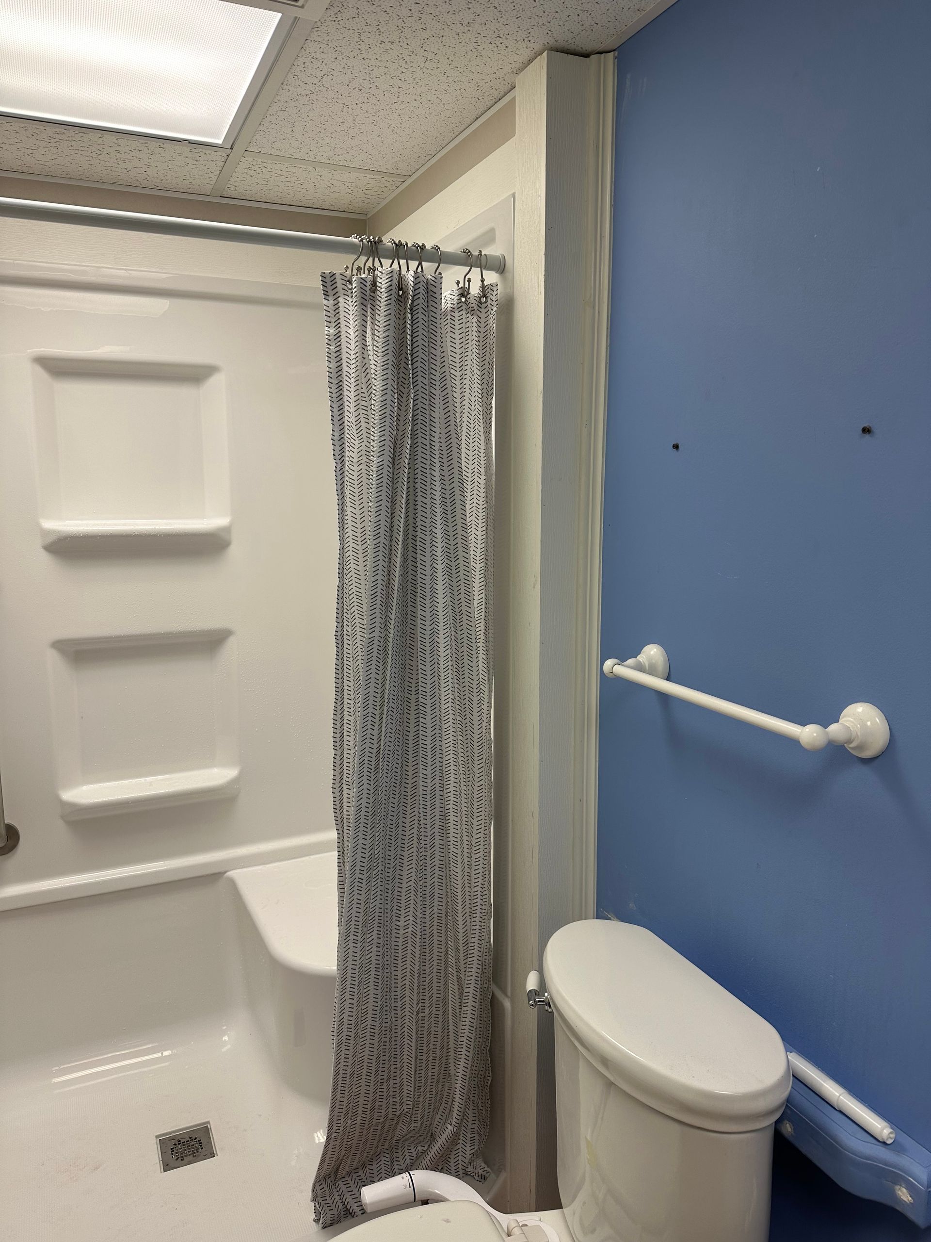 Accessible bathroom with shower-tub, shower curtain, grab bars, and toilet next to blue wall
