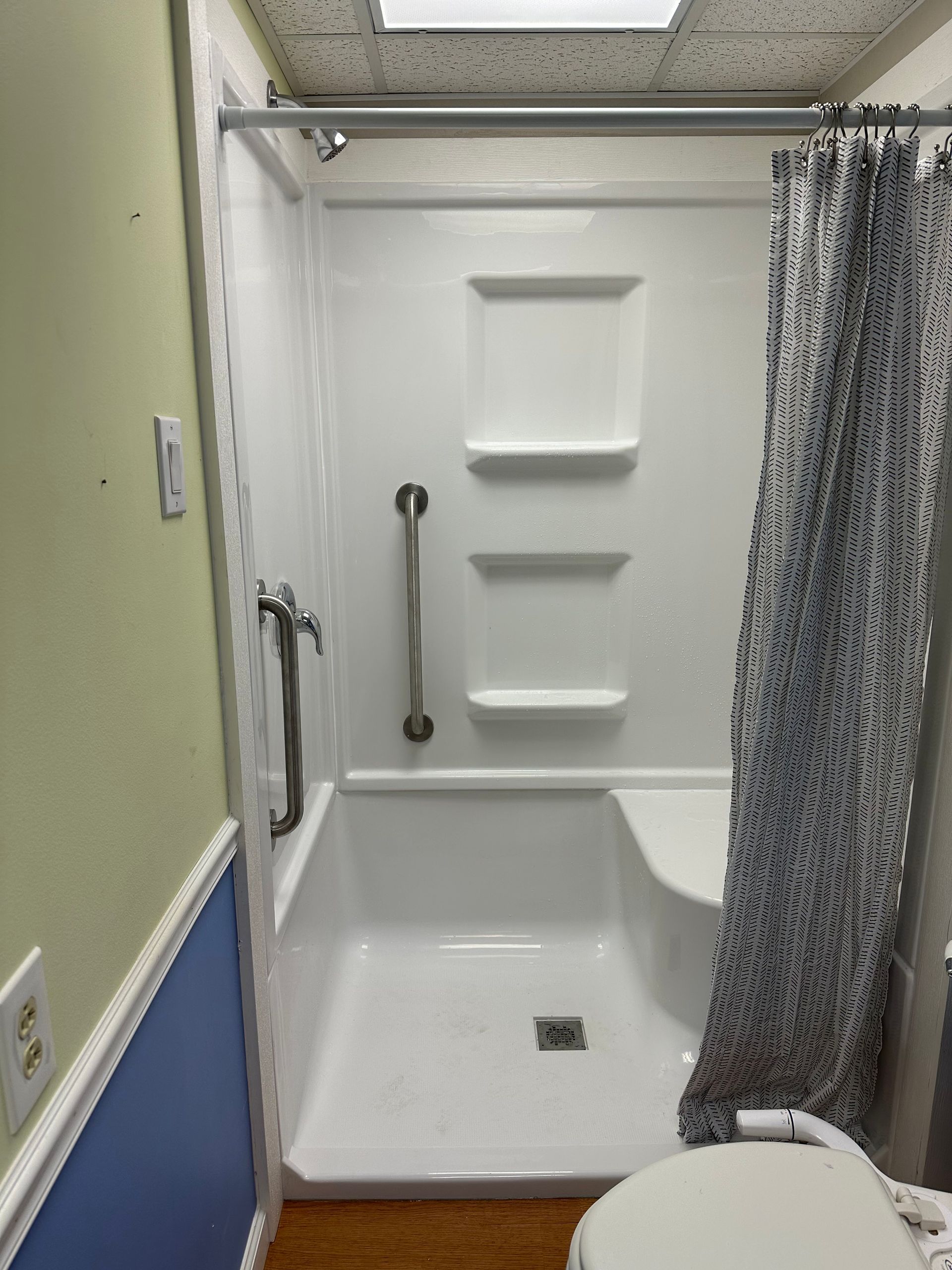 Accessible shower stall with grab bars, built-in seat, and patterned curtain in a bathroom