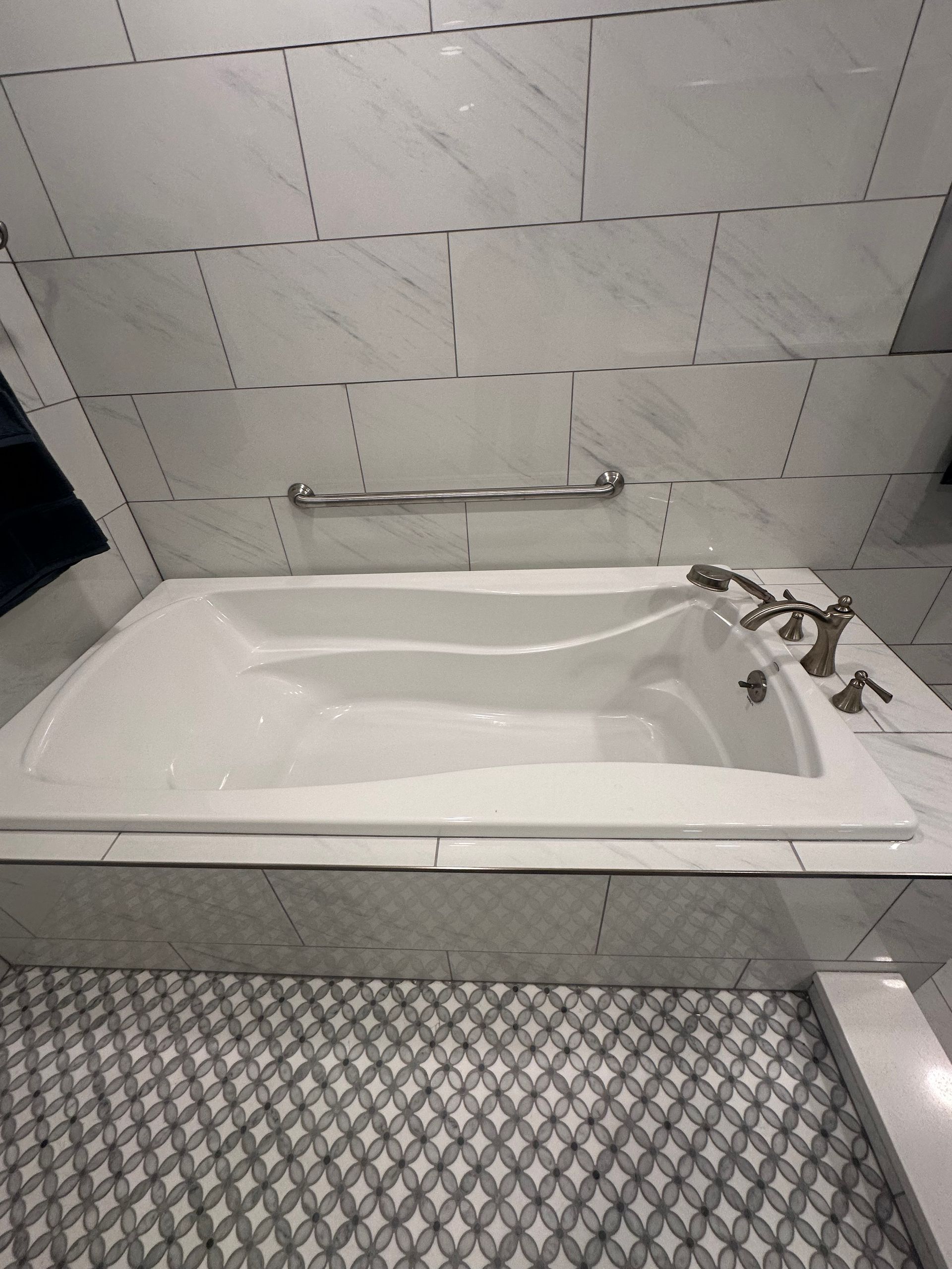 Accessible bathtub with grab bar, handheld shower, and tiled bathroom walls