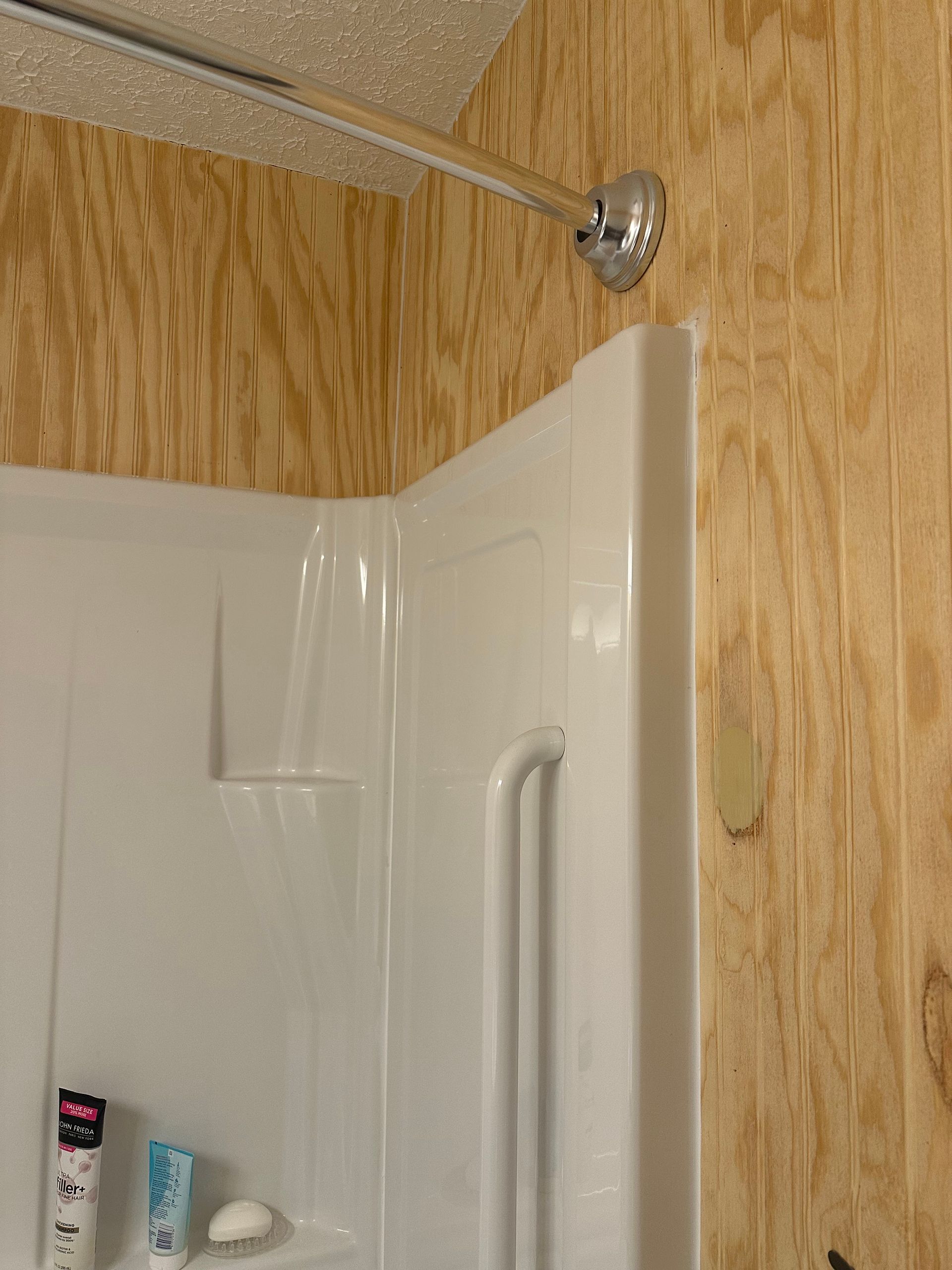 Shower stall with white door, wood-paneled walls, and a chrome showerhead above.