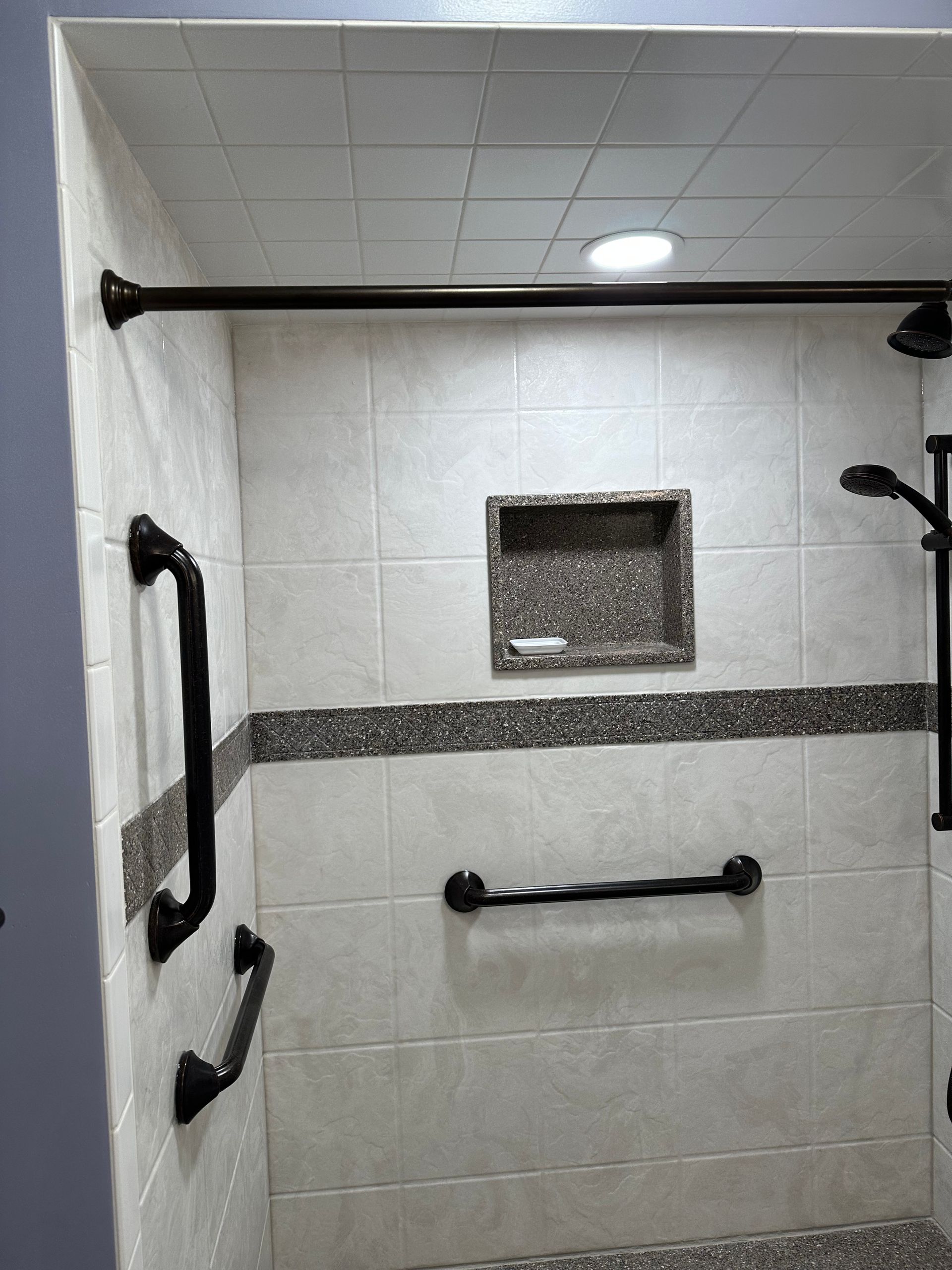 Accessible shower stall with white tile, grab bars, bench, and wall niche.