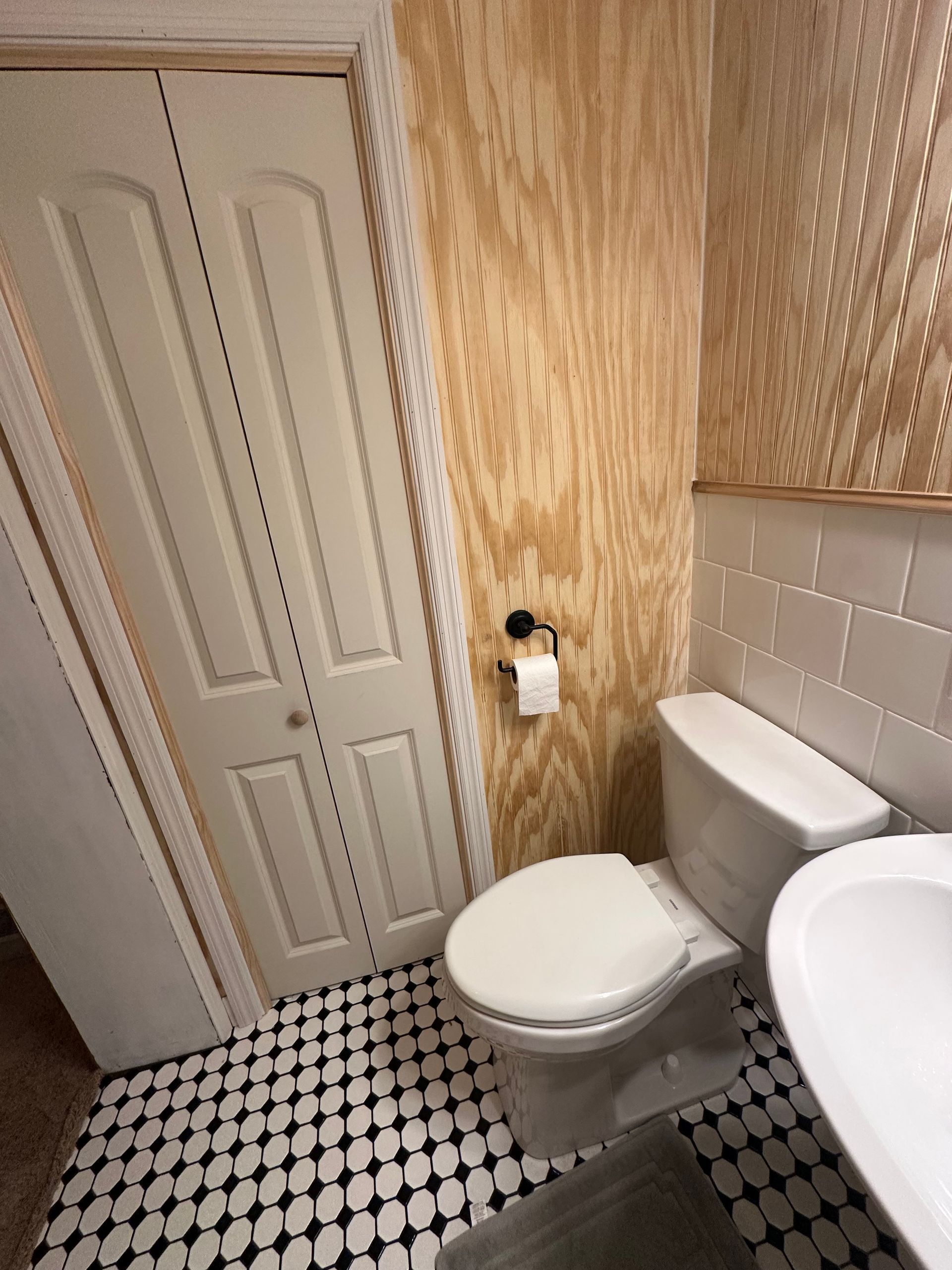 Small bathroom with white toilet, sink, patterned tile floor, and textured beige walls.