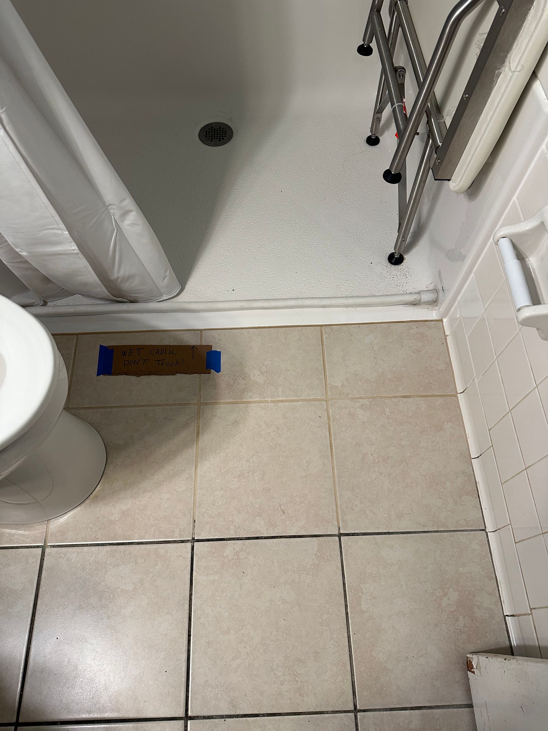 Small bathroom with a shower tray, toilet edge, beige tiled floor, and a metal drying rack.