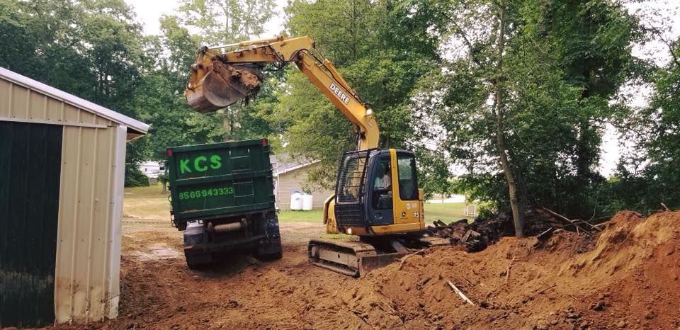 A yellow excavator is loading dirt into a dumpster.