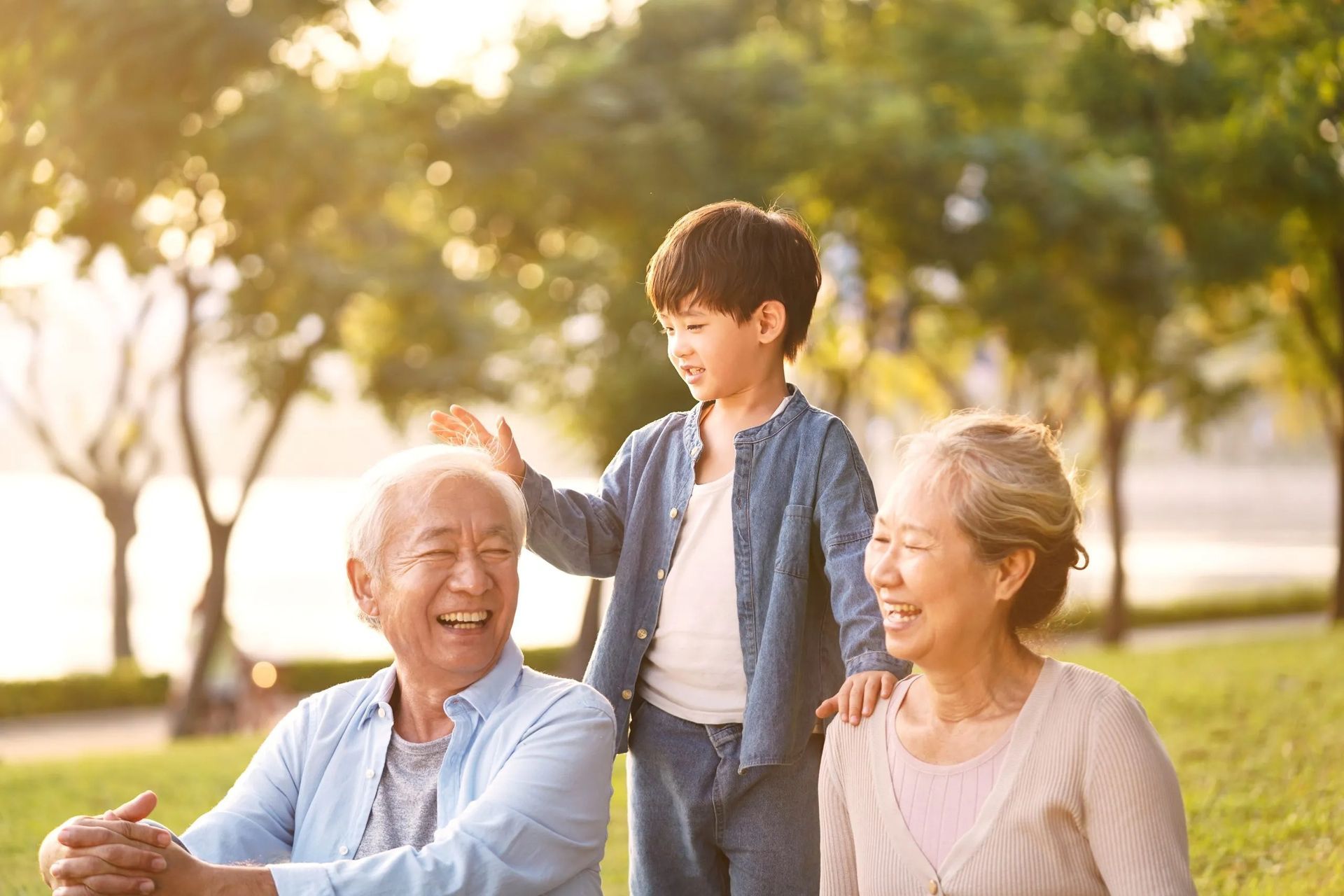 An older couple and a young boy smiling together in a sunlit park.