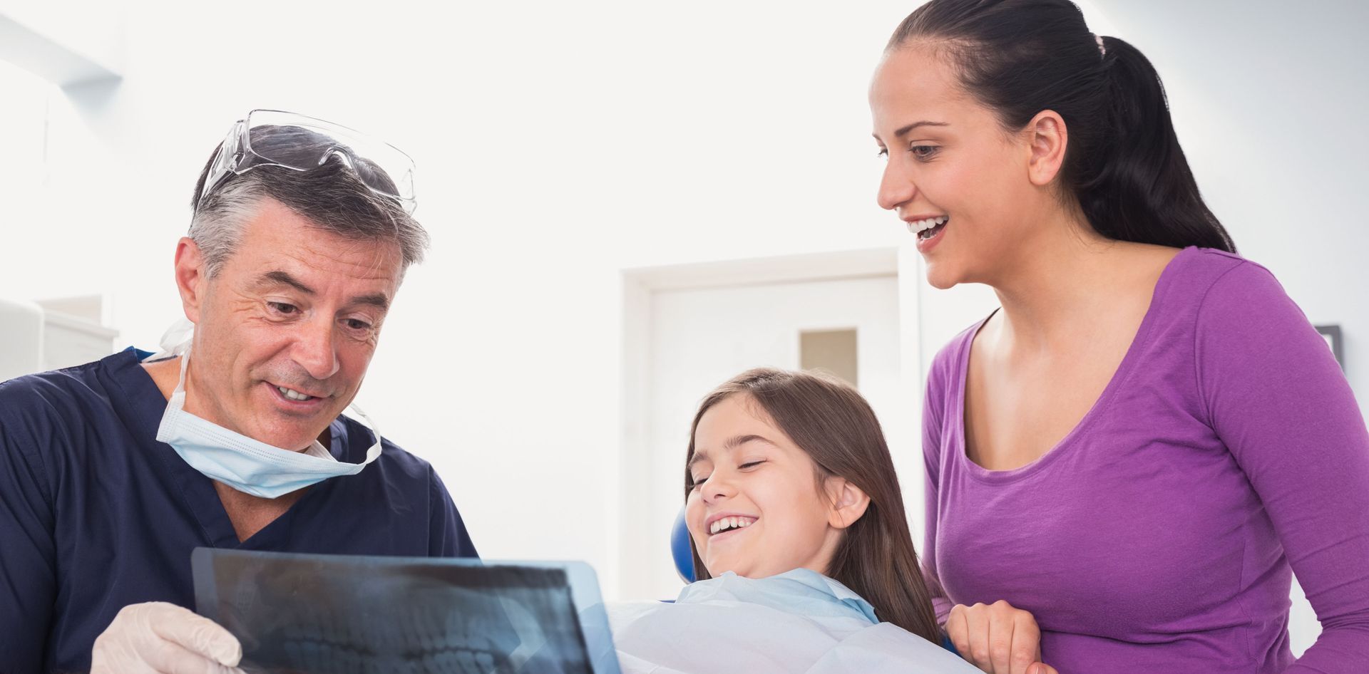 A dentist showing a dental X-ray to a patient and a parent in a clinical office.